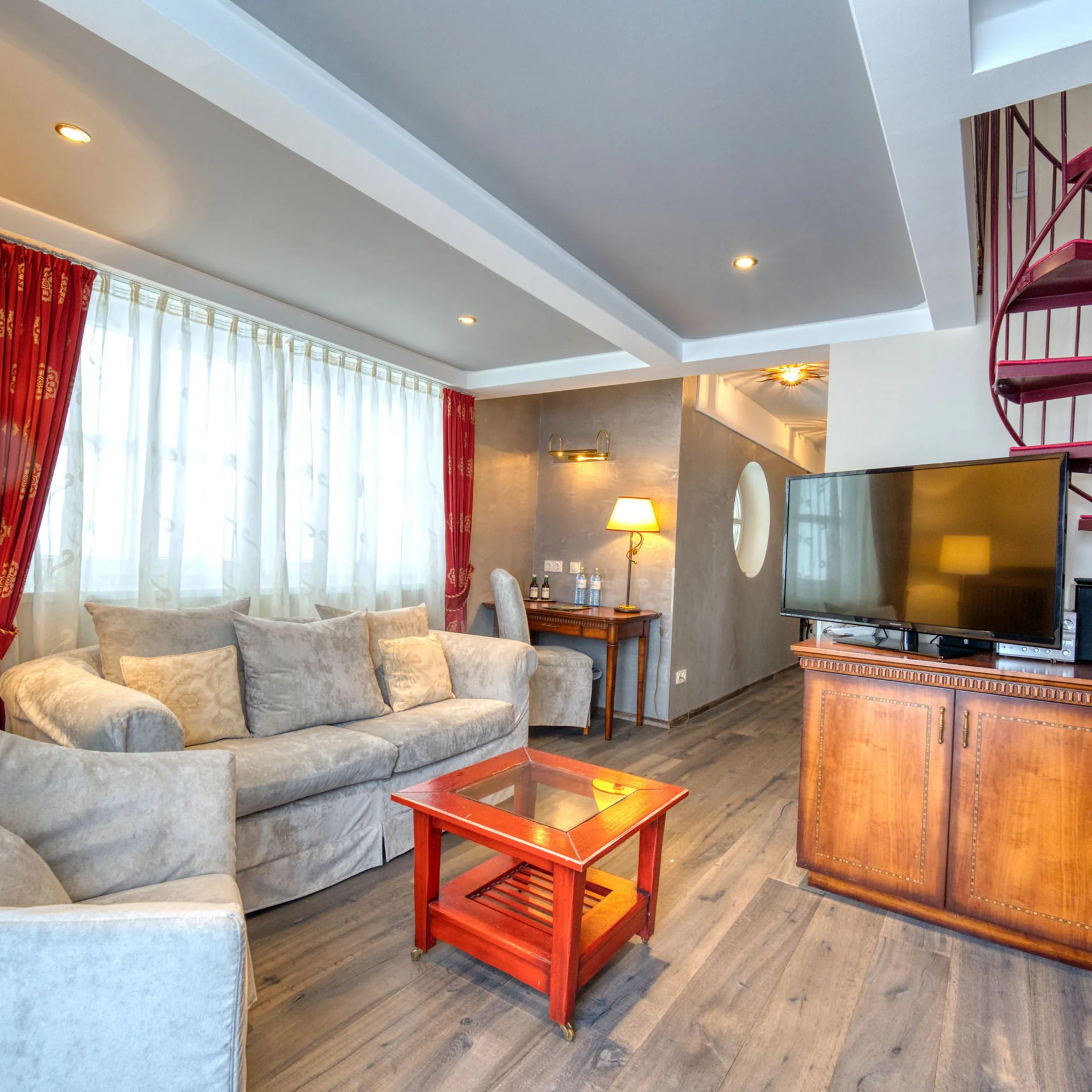 Wohnzimmer mit grauen Sofas, rotem Beistelltisch und roter Wendeltreppe
