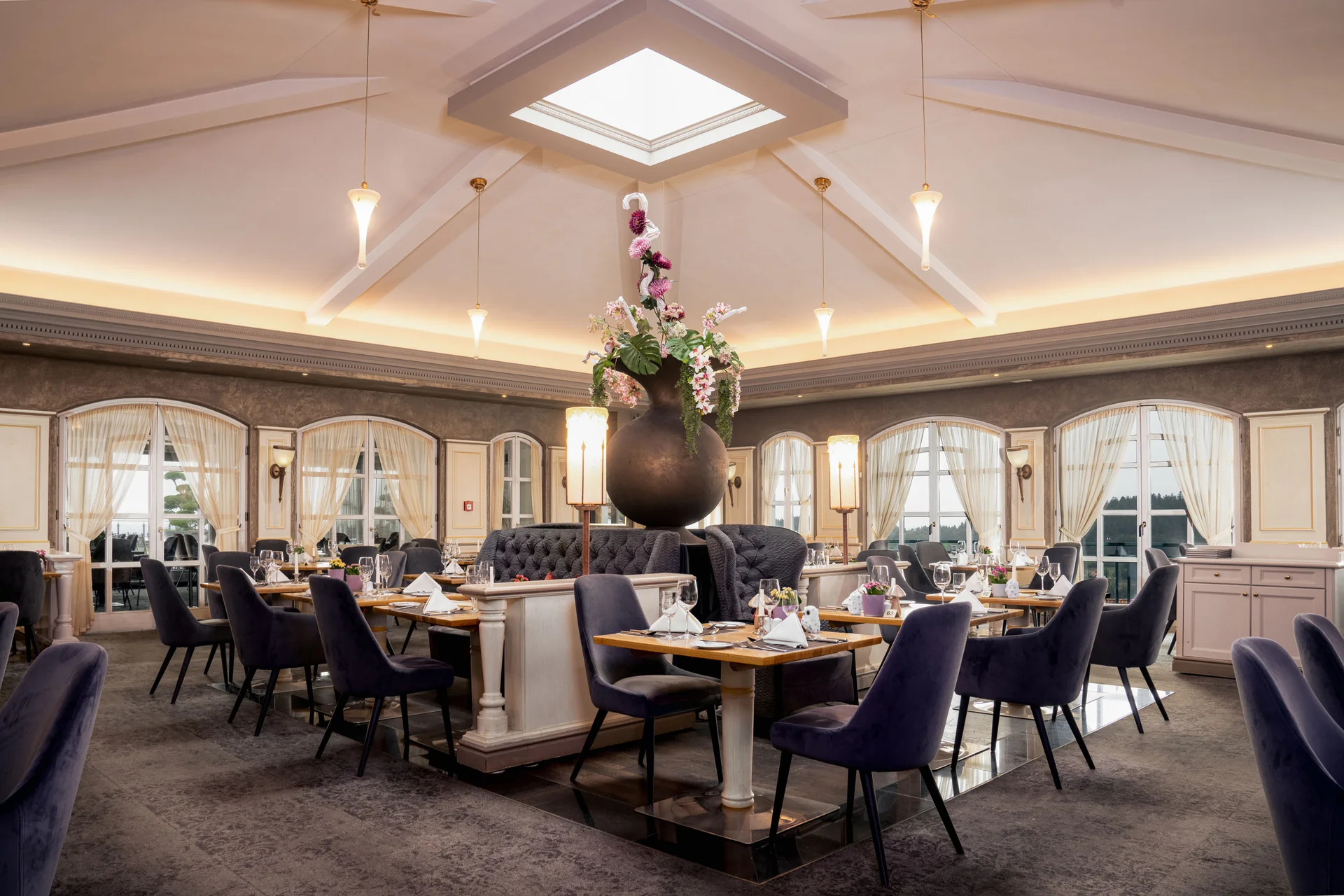 Elegantes Restaurant mit hohen Fenstern und großer Blumenvase in der Mitte