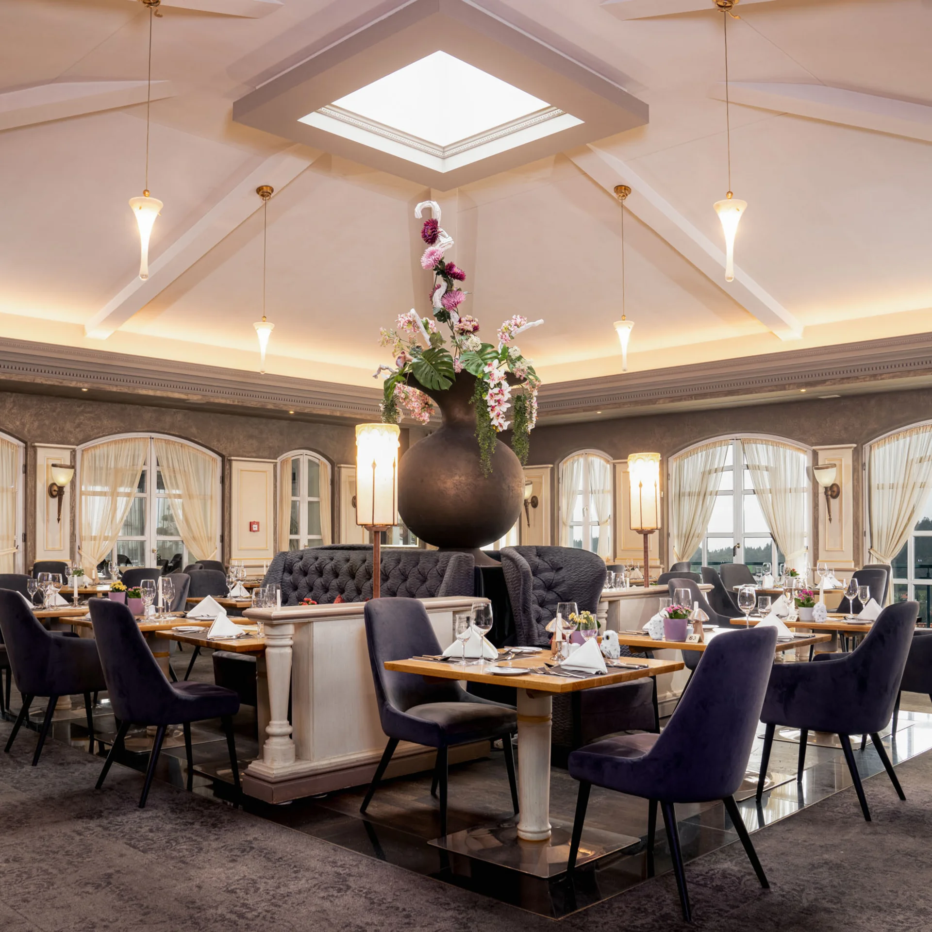 Elegantes Restaurant mit hohen Fenstern und großer Blumenvase in der Mitte