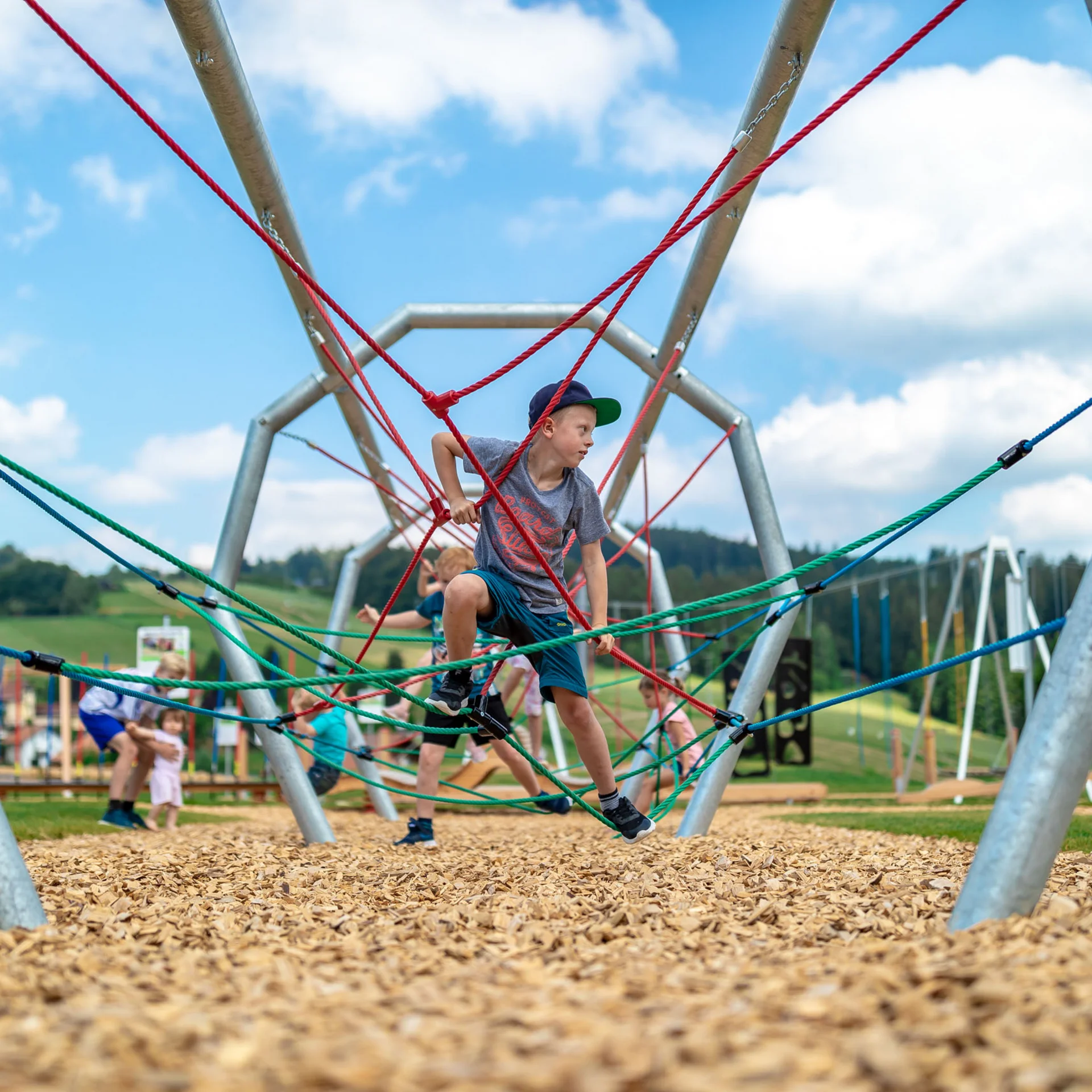 Junge klettert auf Klettergerüst im Spielplatz bei sonnigem Wetter