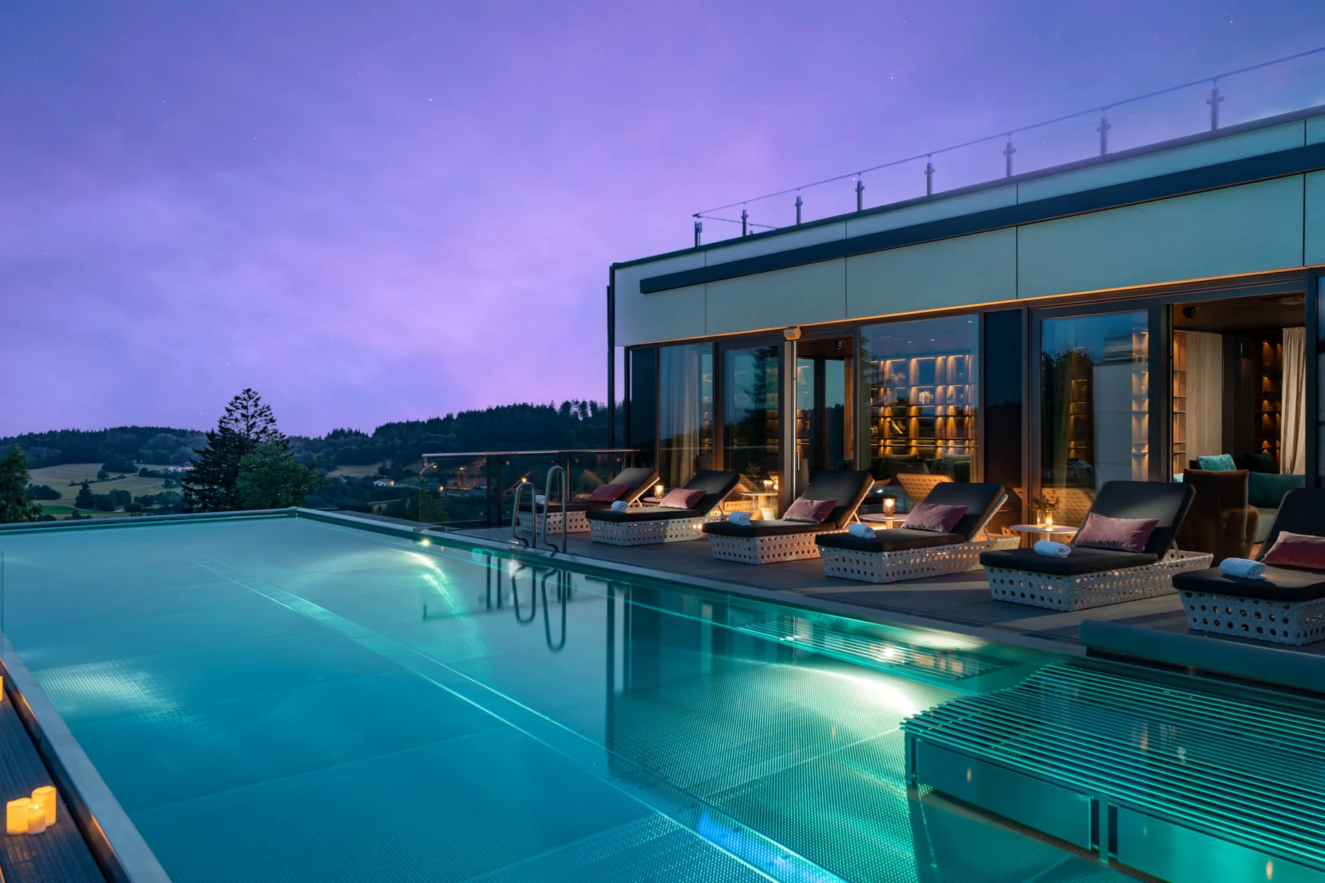Modernes Gebäude mit beleuchtetem Pool und Liegestühlen bei Abenddämmerung