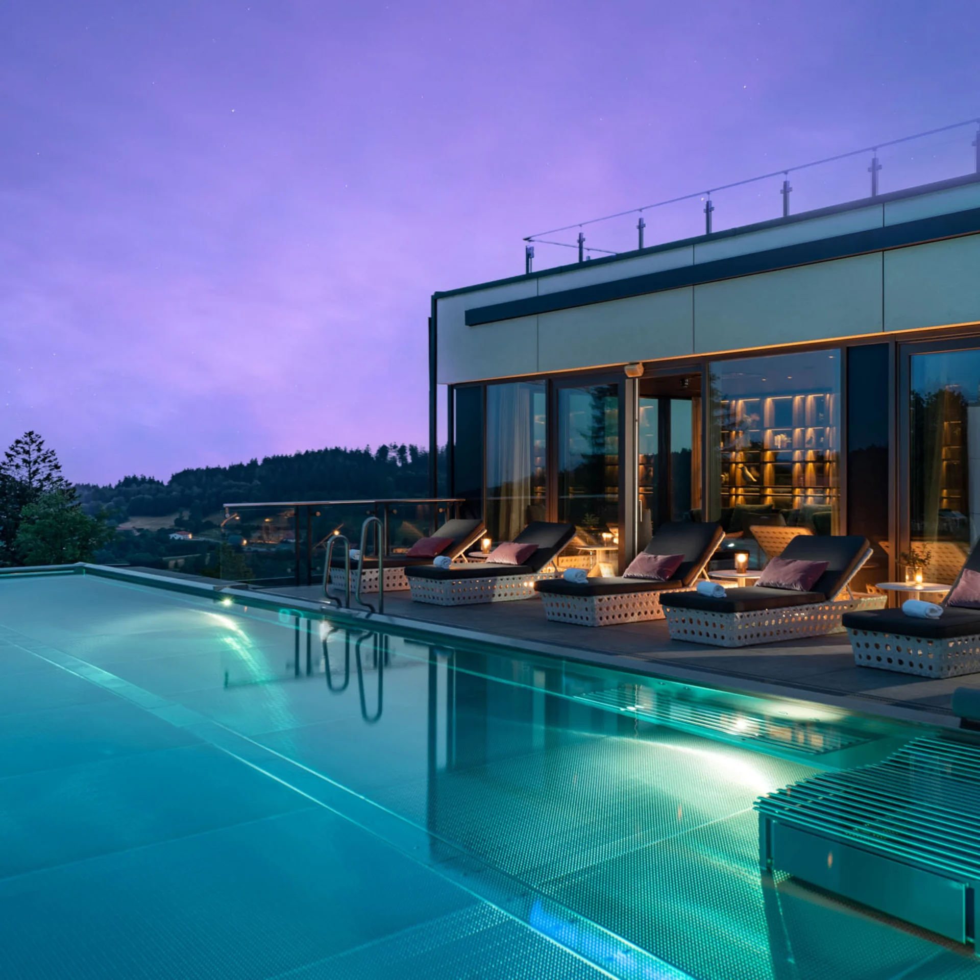 Modernes Gebäude mit beleuchtetem Pool und Liegestühlen bei Abenddämmerung