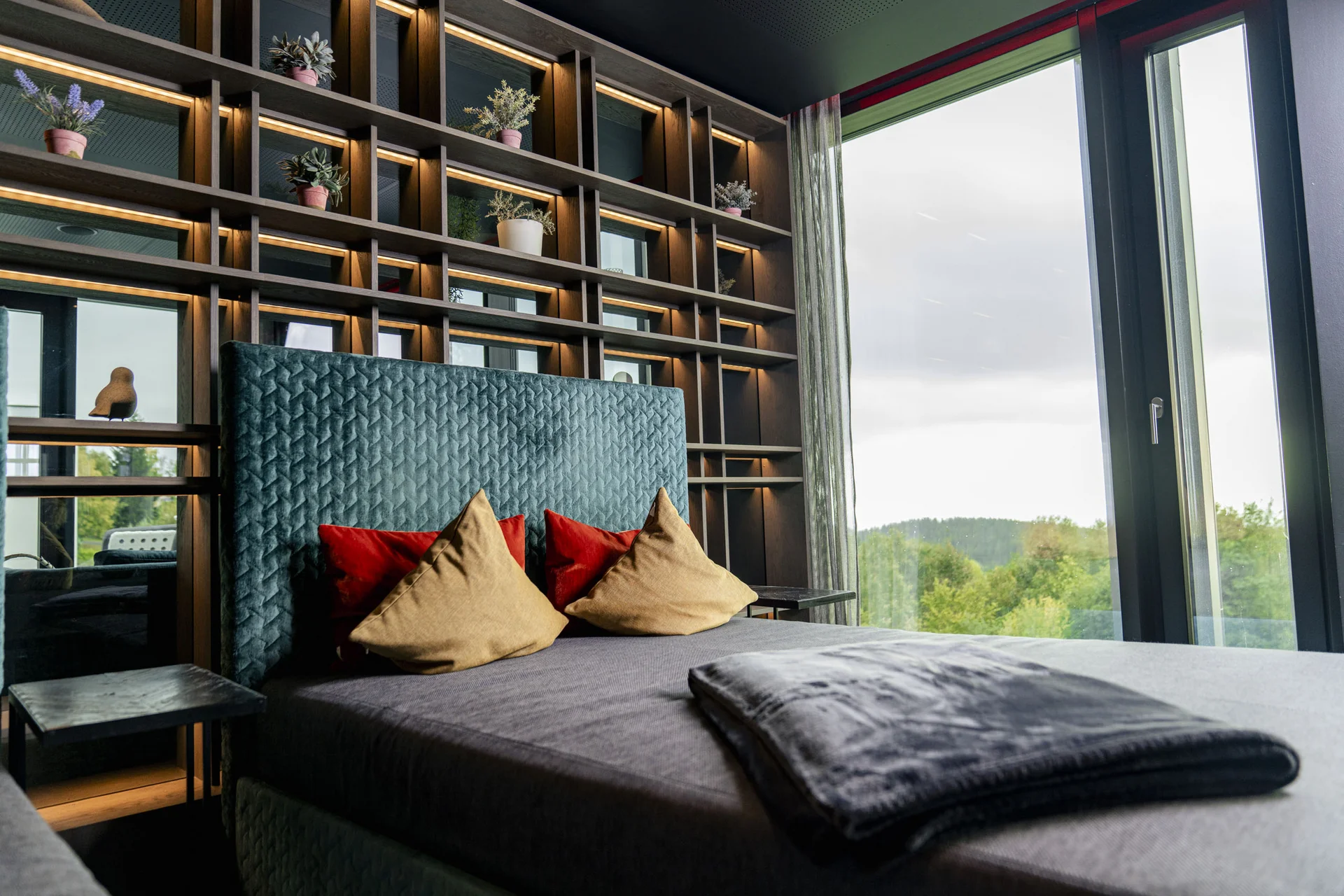 Modernes Schlafzimmer mit beleuchtetem Regal und großen Fenstern mit Naturblick