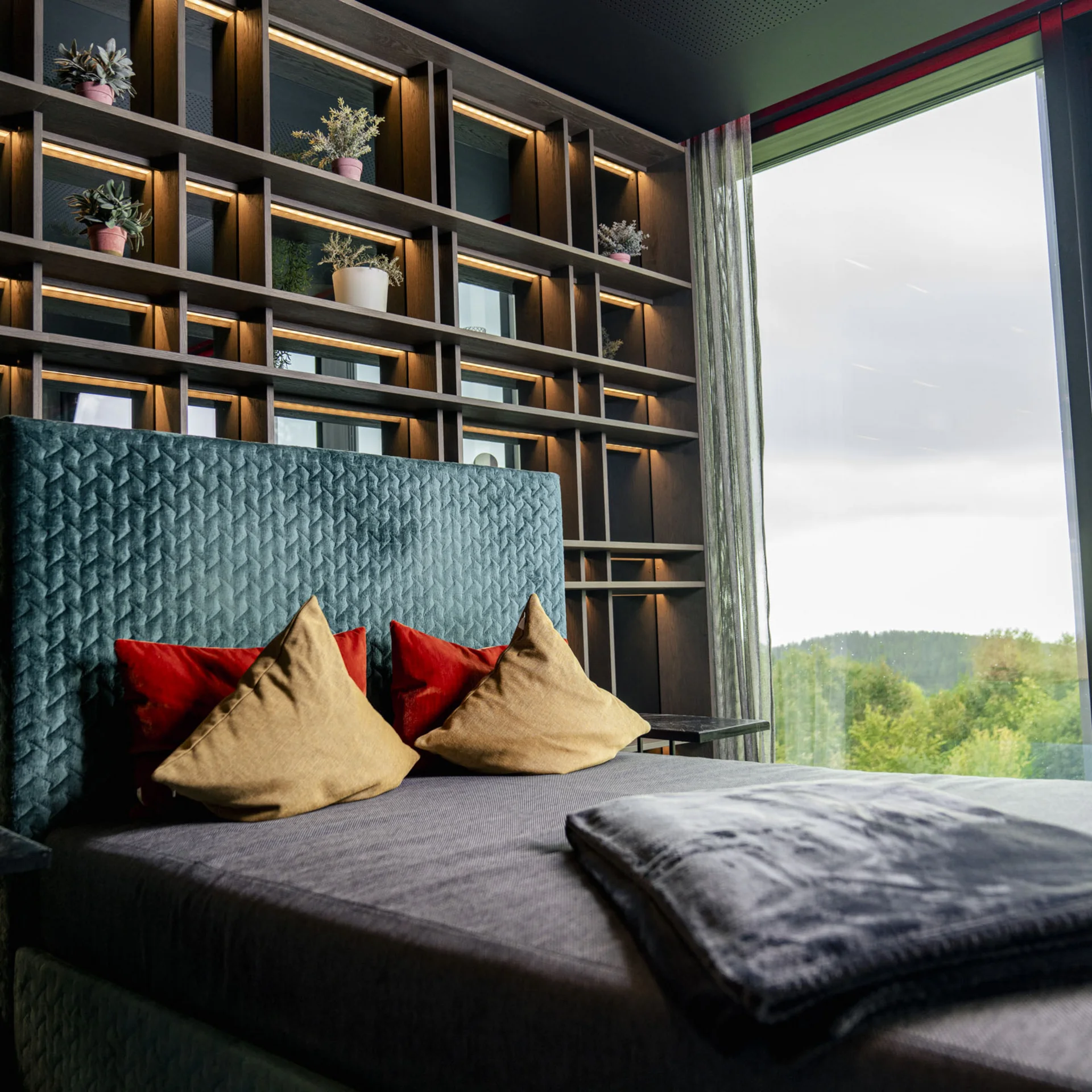 Modernes Schlafzimmer mit beleuchtetem Regal und großen Fenstern mit Naturblick