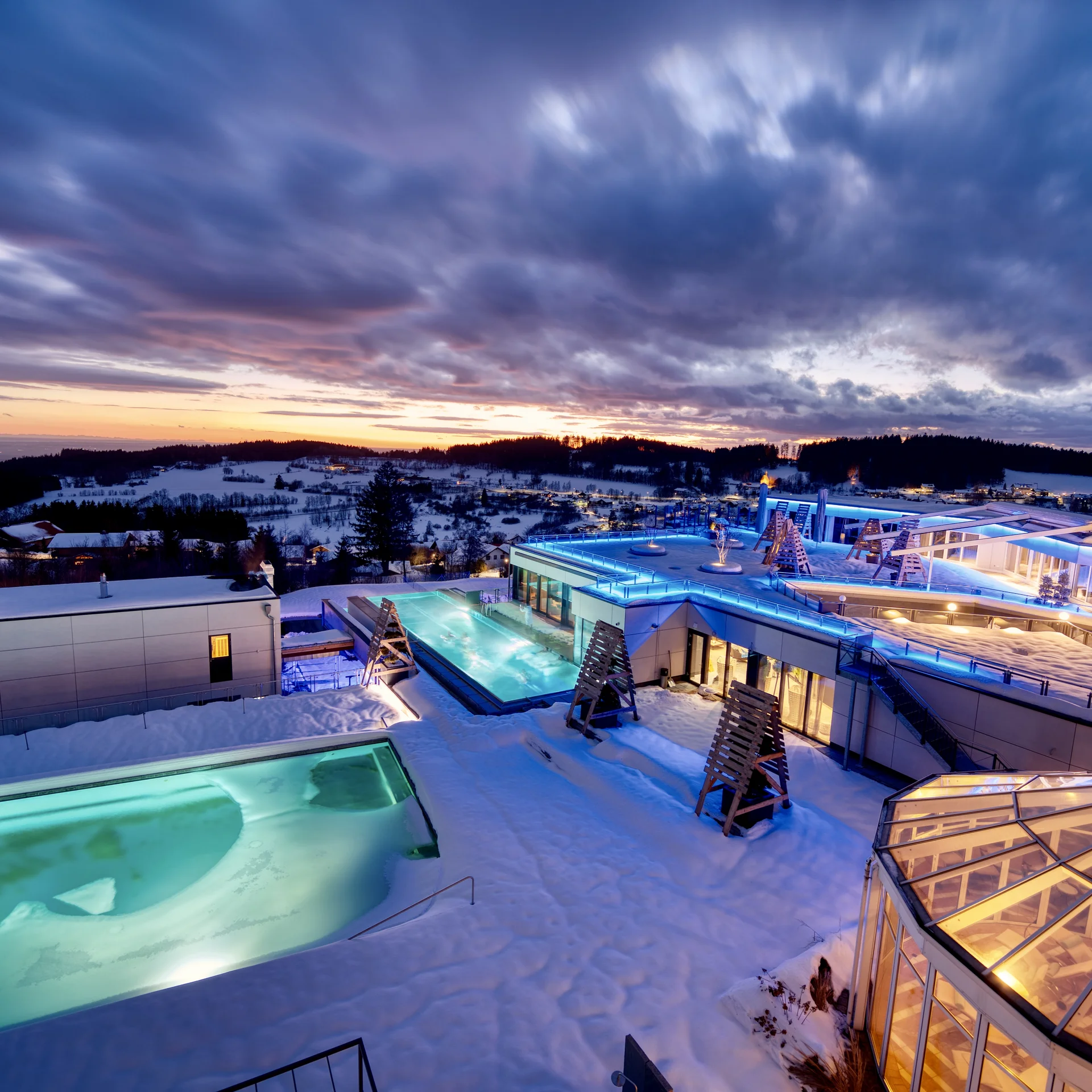 Moderner Spa mit beleuchteten Pools bei Sonnenuntergang in verschneiter Landschaft