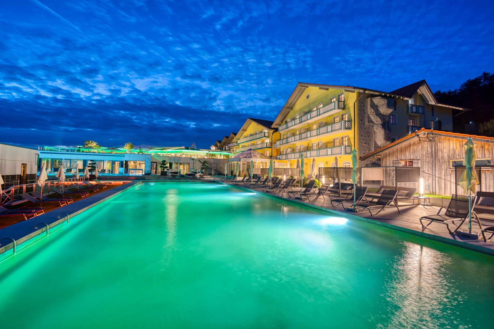 Beleuchtetes Schwimmbecken vor einem Hotel bei Nacht unter blauem Himmel