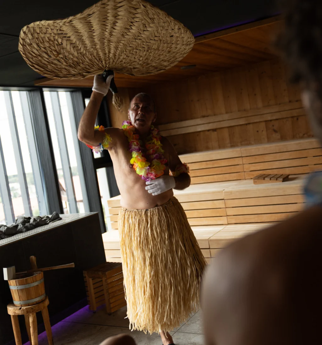 Mann im Hawaii-Kostüm wedelt mit geflochtenem Fächer in Sauna
