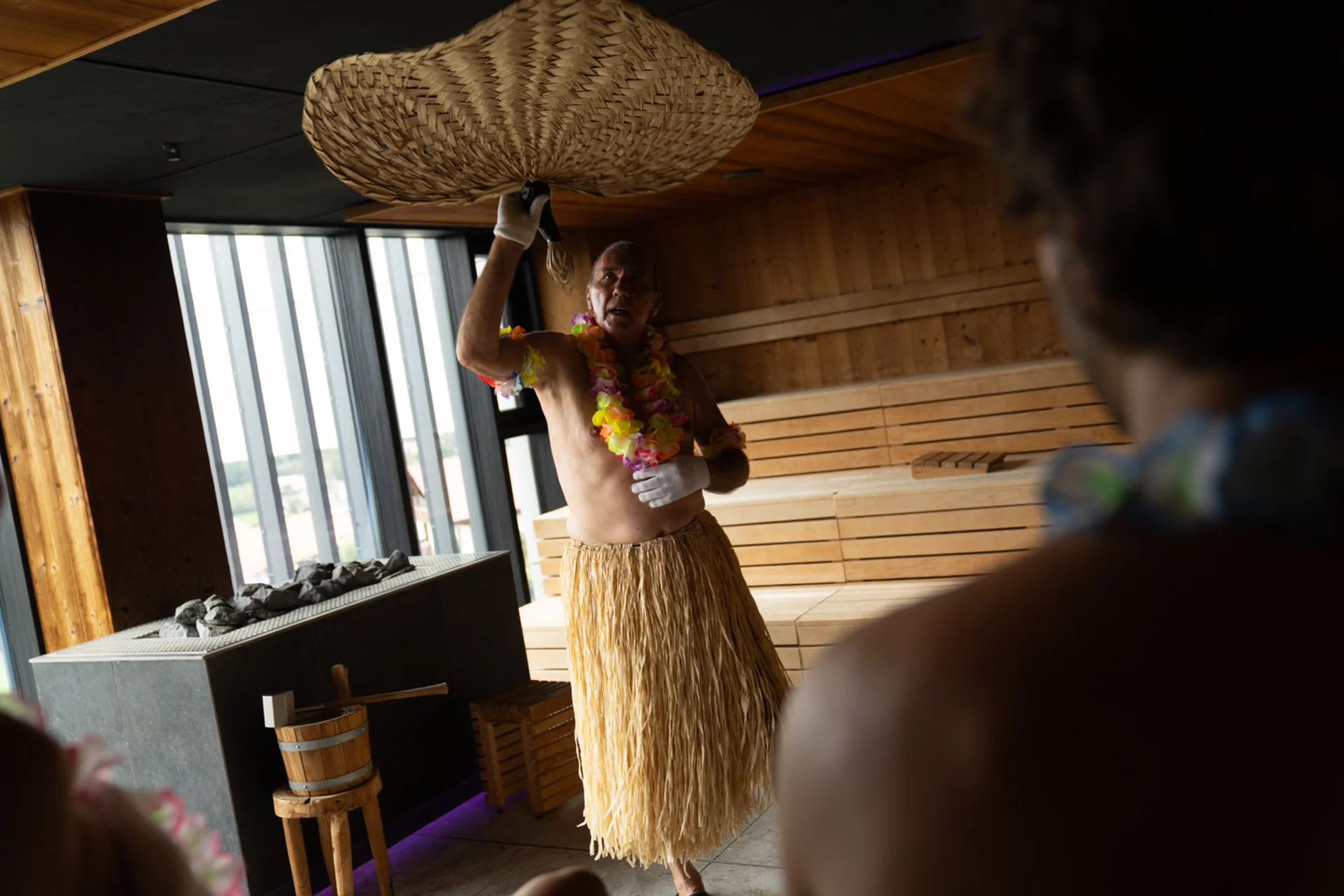 Mann im Hawaii-Kostüm wedelt mit geflochtenem Fächer in Sauna