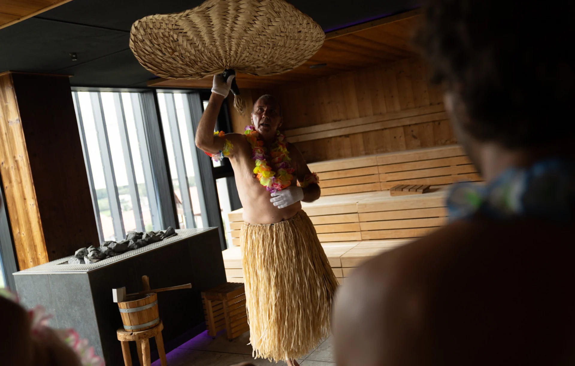 Mann im Hawaii-Kostüm wedelt mit geflochtenem Fächer in Sauna