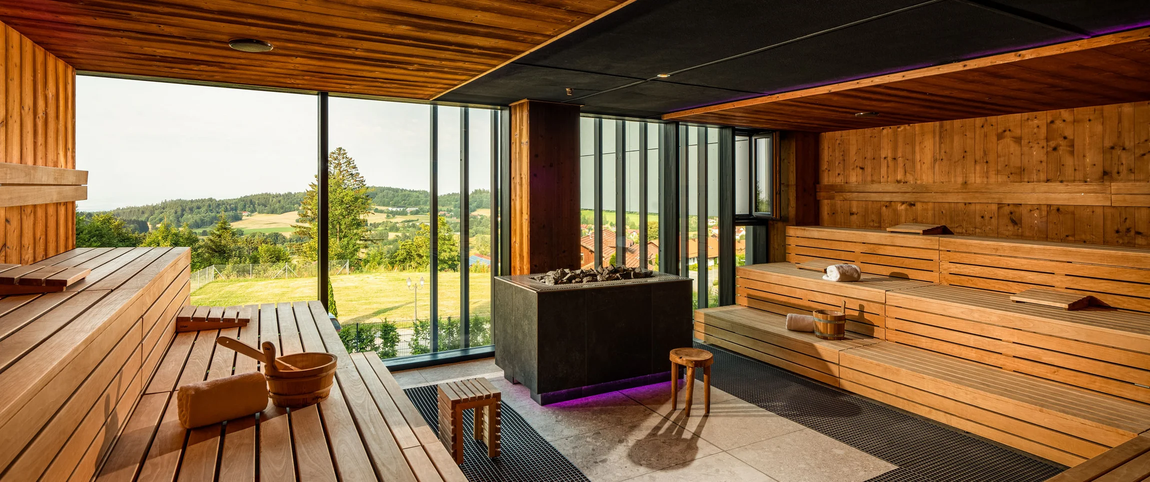 Moderne Sauna mit Holzvertäfelung und Panoramafenster mit Aussicht auf grüne Landschaft