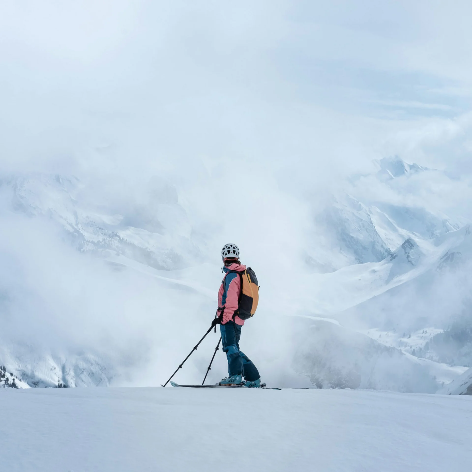 Skifahrer steht auf verschneitem Berg mit Aussicht auf Wolken und Gipfel