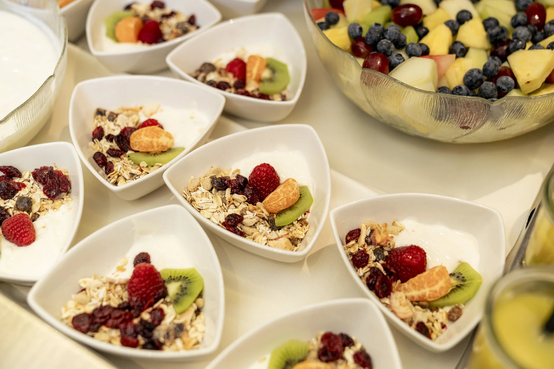 Schalen mit Müsli, Joghurt und frischem Obst sowie ein großer Obstsalat
