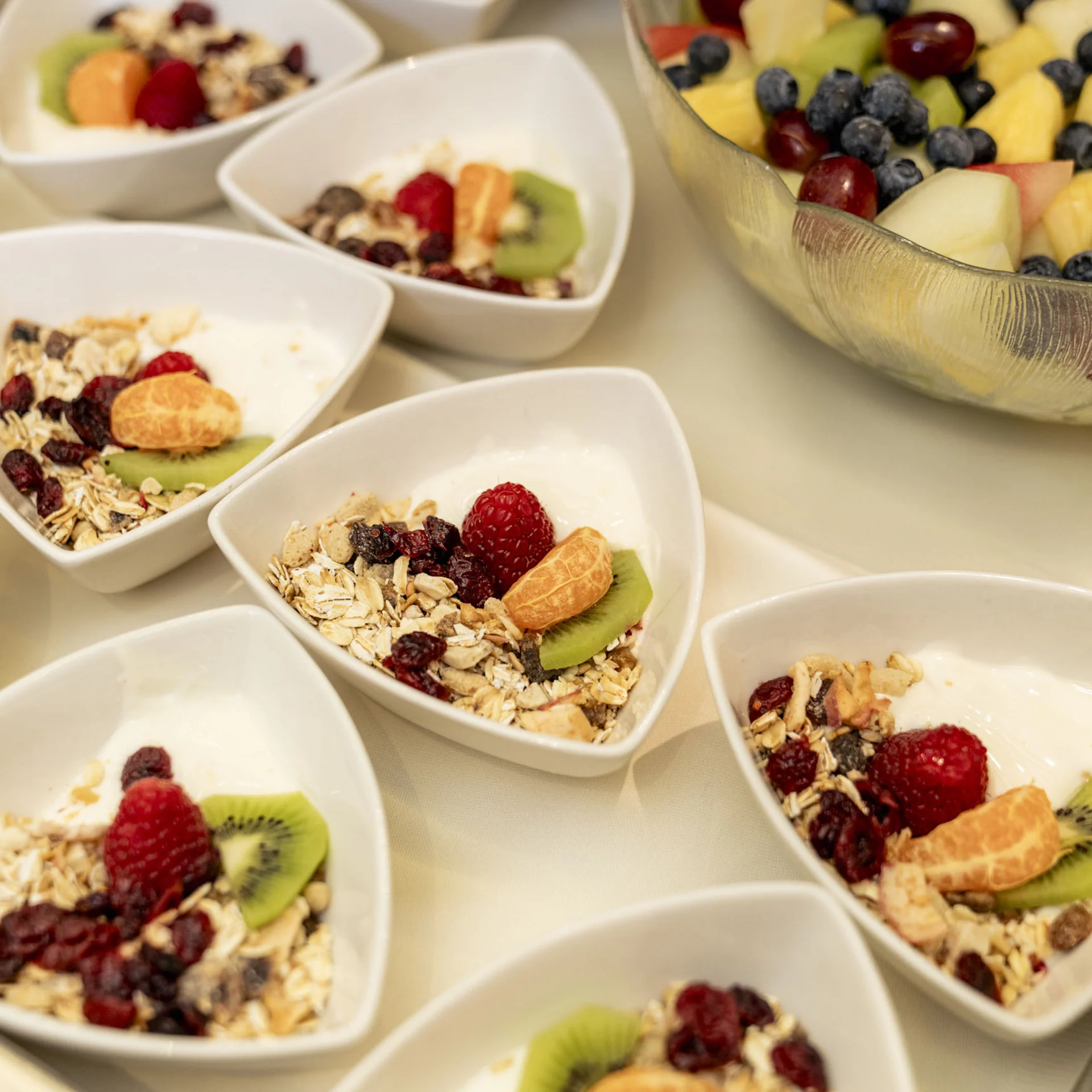 Schalen mit Müsli, Joghurt und frischem Obst sowie ein großer Obstsalat