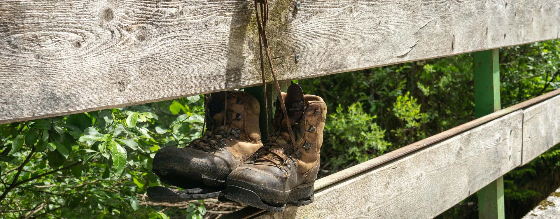Abgenutzte Wanderschuhe hängen an einem Holzgeländer im Wald