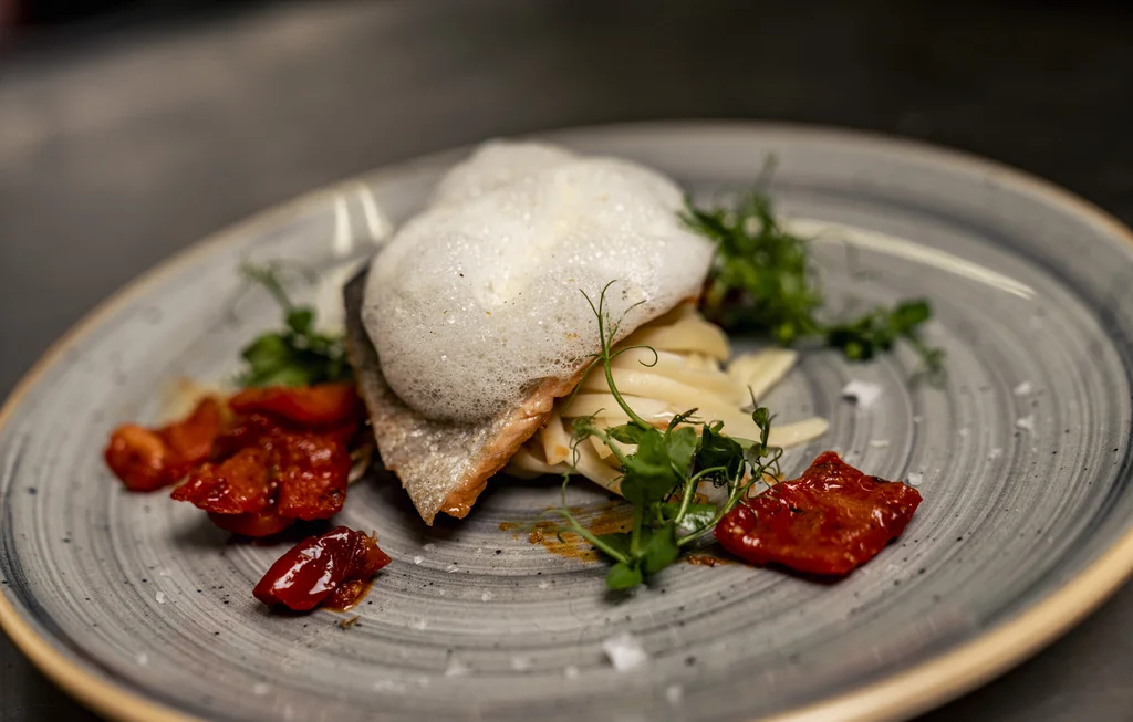 Für Feiern in kleiner und großer Runde Gebratenes Fischfilet mit Schaum, Kräutern und gerösteten Tomaten auf einem grauen Teller