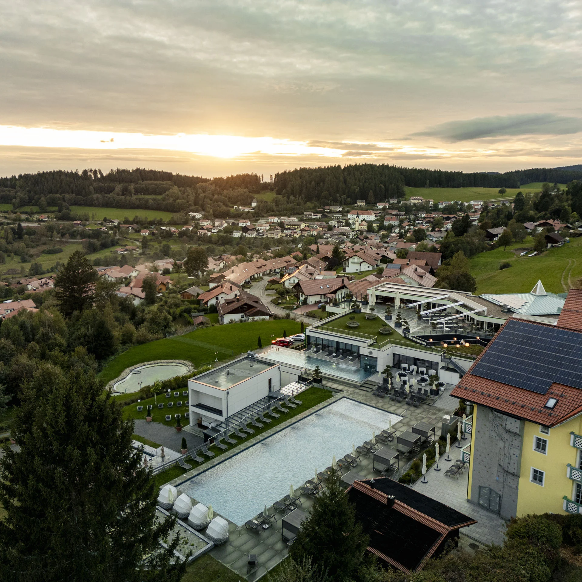 Luftaufnahme eines Hotels mit Pool in einer grünen Hügellandschaft bei Sonnenuntergang