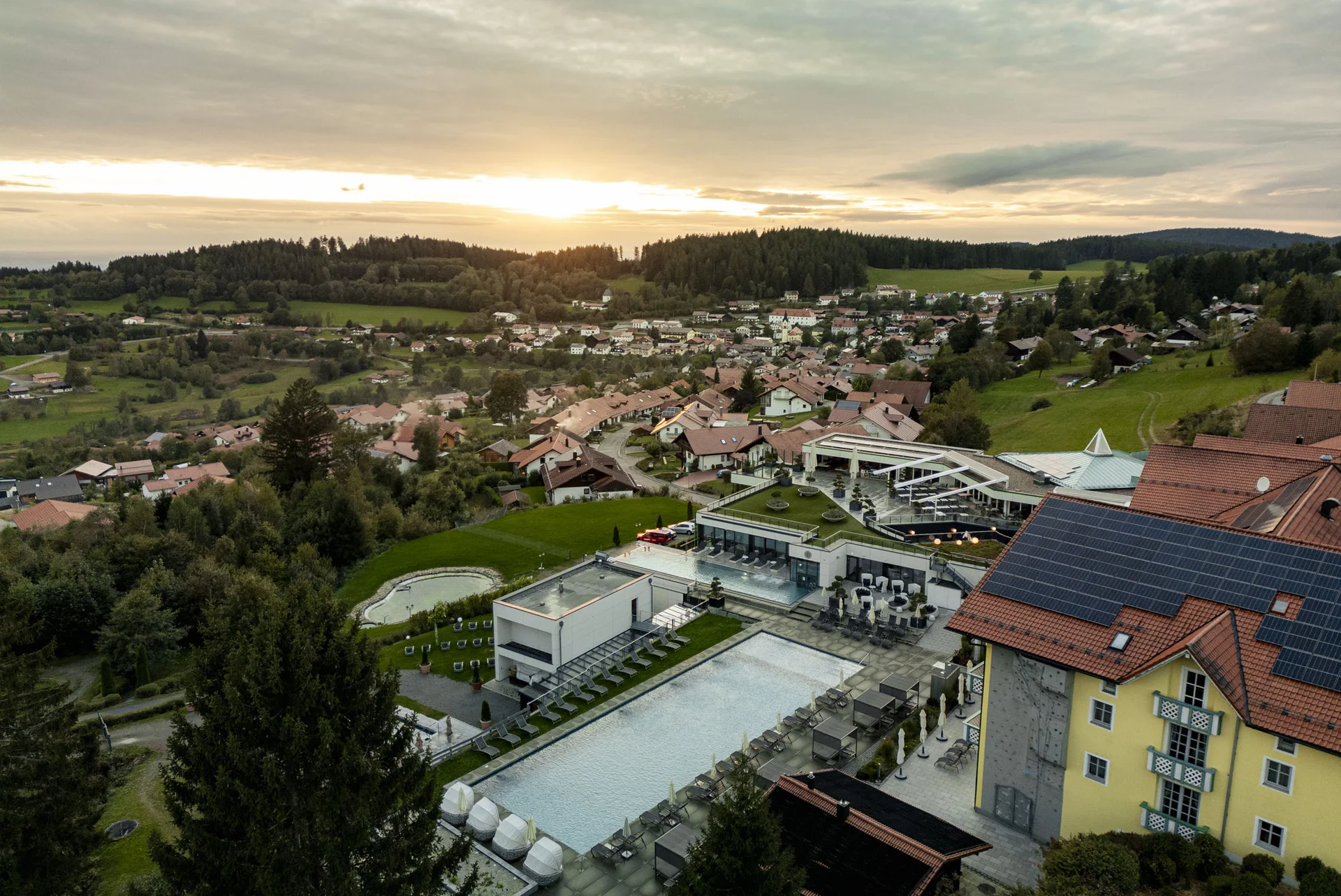 Angerhof: Urlaub in Panoramalage im Bayerischen Wald Luftaufnahme eines Hotels mit Pool in einer grünen Hügellandschaft bei Sonnenuntergang
