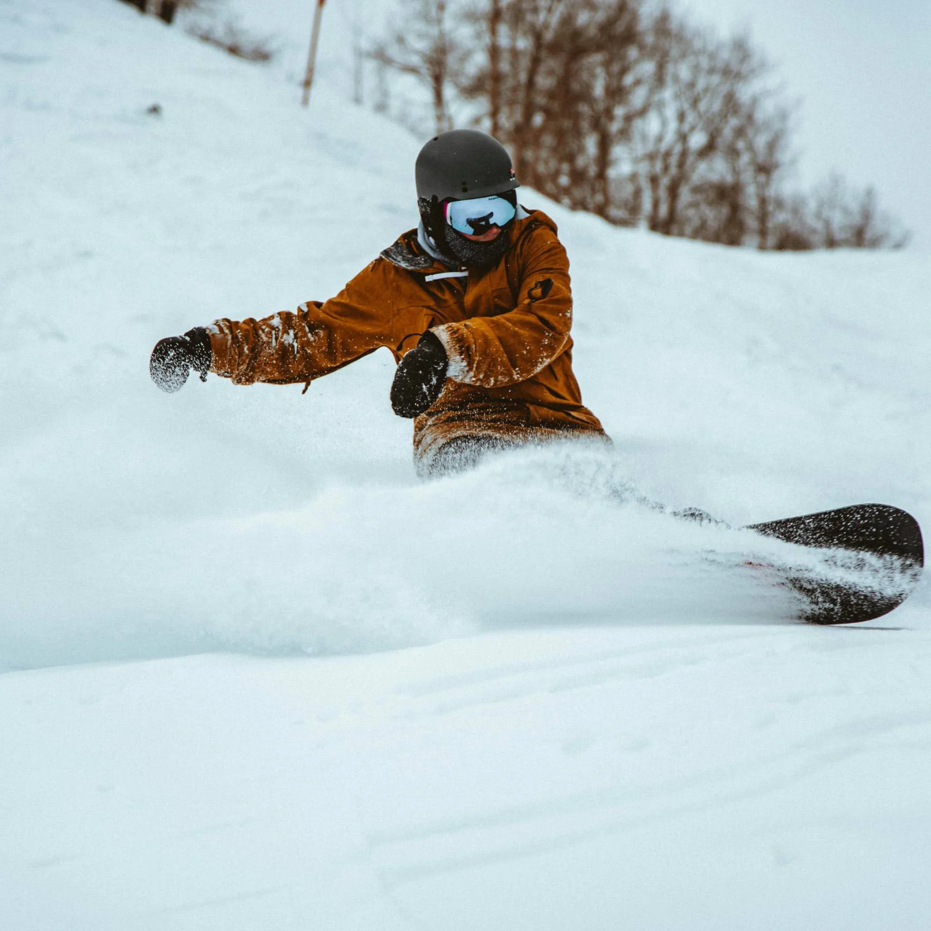 Snowboarder in brauner Jacke fährt im tiefen Schnee