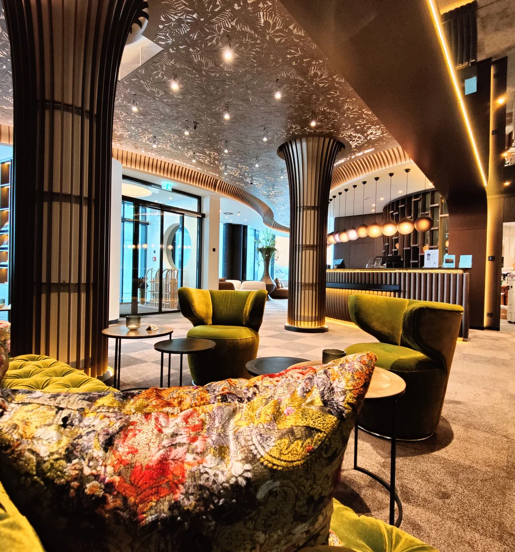Die Adresse für Wellness in Bayern: Ihr Hotel in St. Englmar Moderne Hotellobby mit grünen Sesseln und kunstvoll verziertem Deckengewölbe.