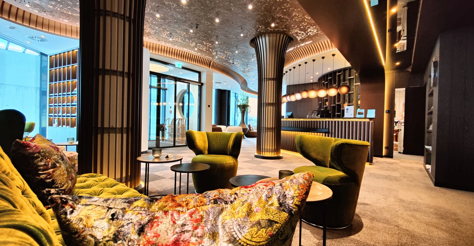 Moderne Hotellobby mit grünen Sesseln und kunstvoll verziertem Deckengewölbe.