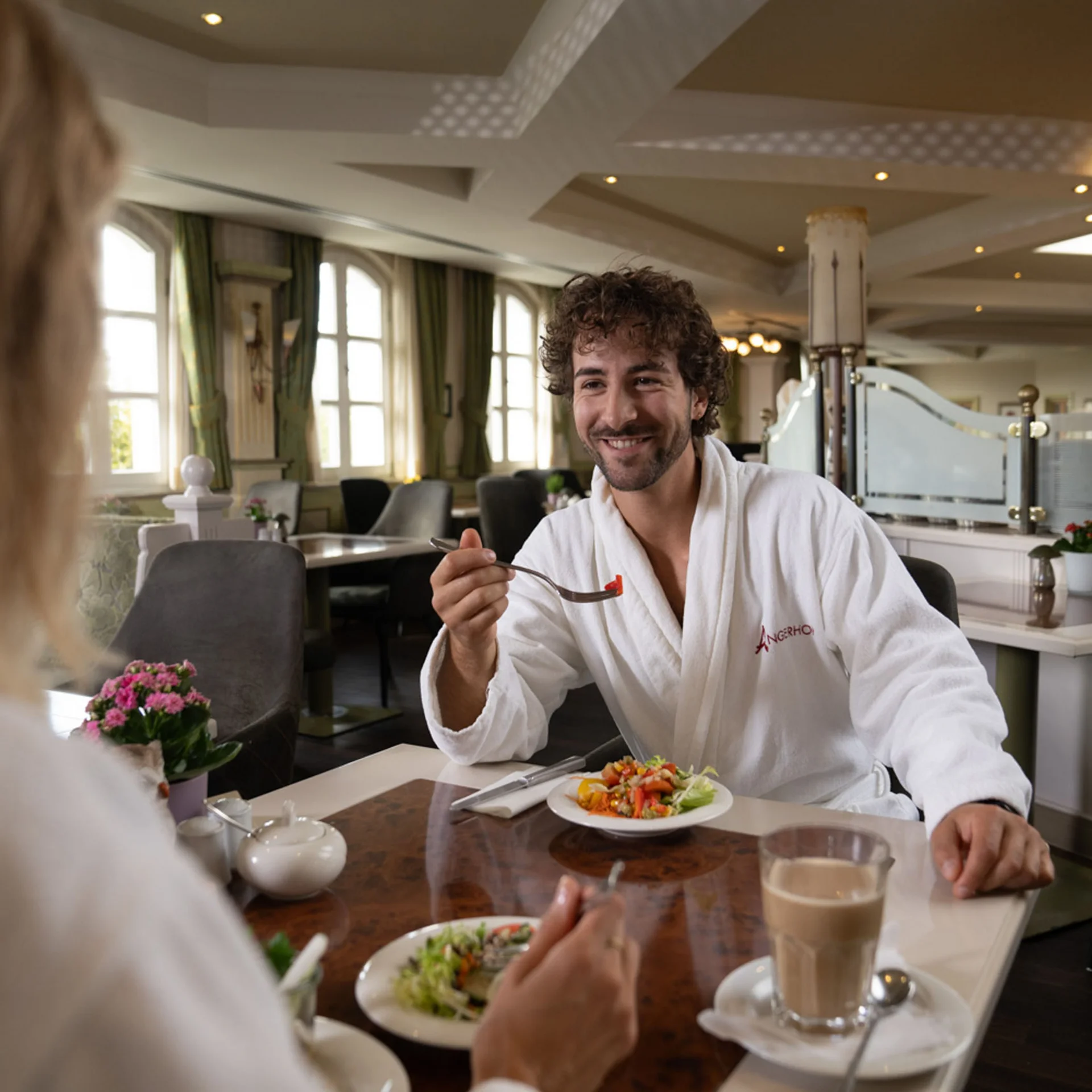 Mann in Bademantel isst Salat in elegantem Restaurant