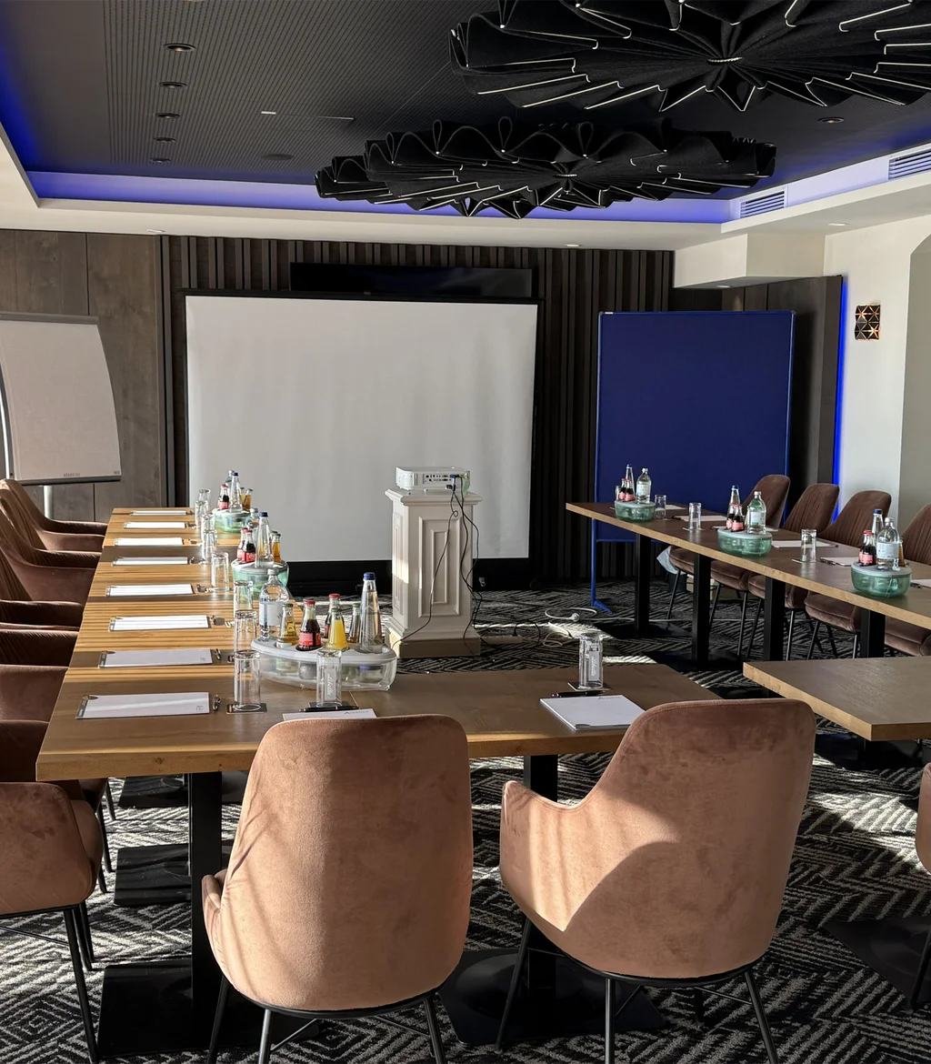 Die passenden Räumlichkeiten für Ihre Ziele Modern eingerichteter Konferenzraum mit Tisch, Stühlen und Präsentationsfläche