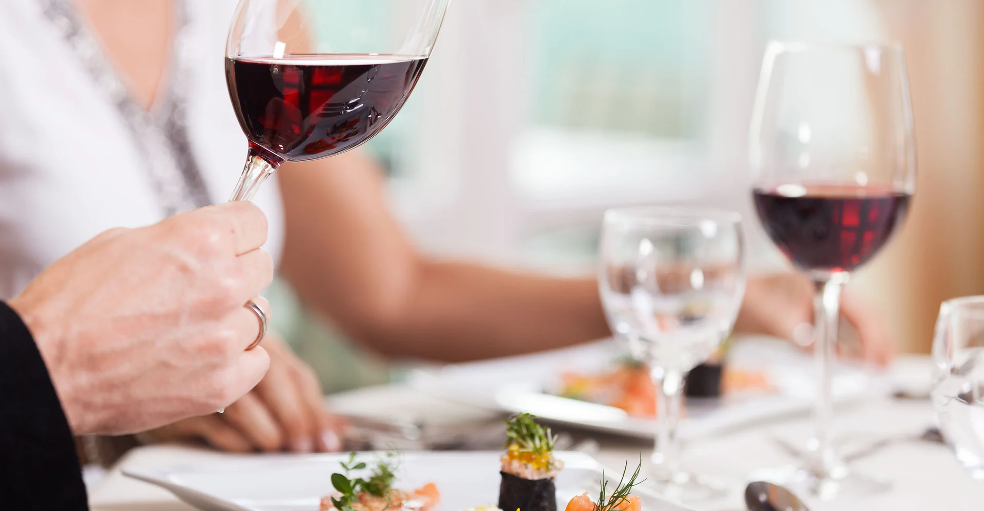 Person hält ein Glas Rotwein über einem Teller mit feinem Essen