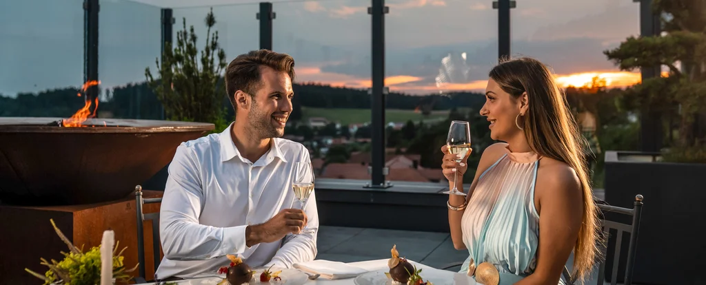 Paar genießt Abendessen und Champagner auf Terrasse bei Sonnenuntergang
