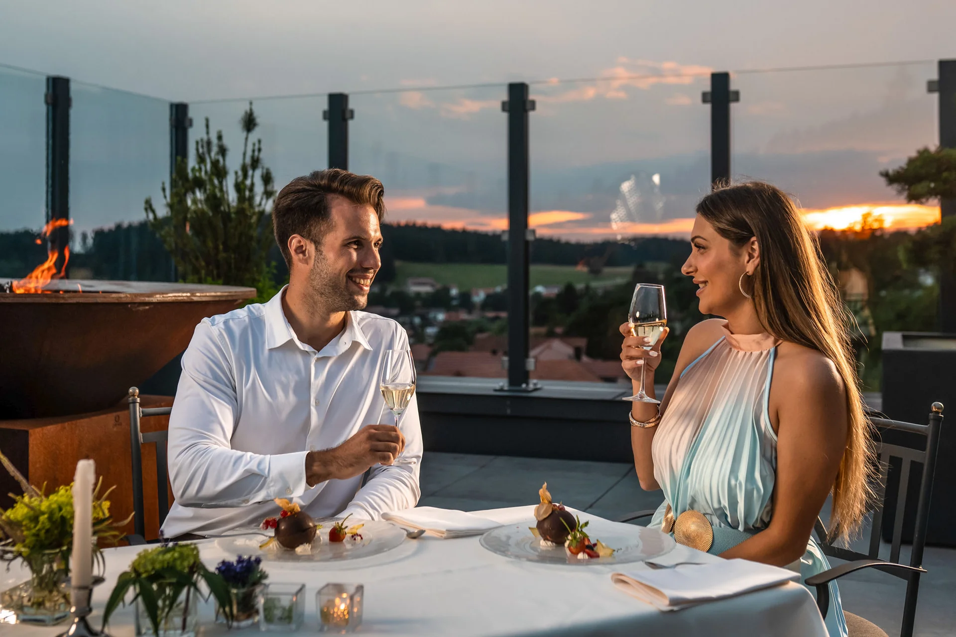 Paar genießt Abendessen und Champagner auf Terrasse bei Sonnenuntergang