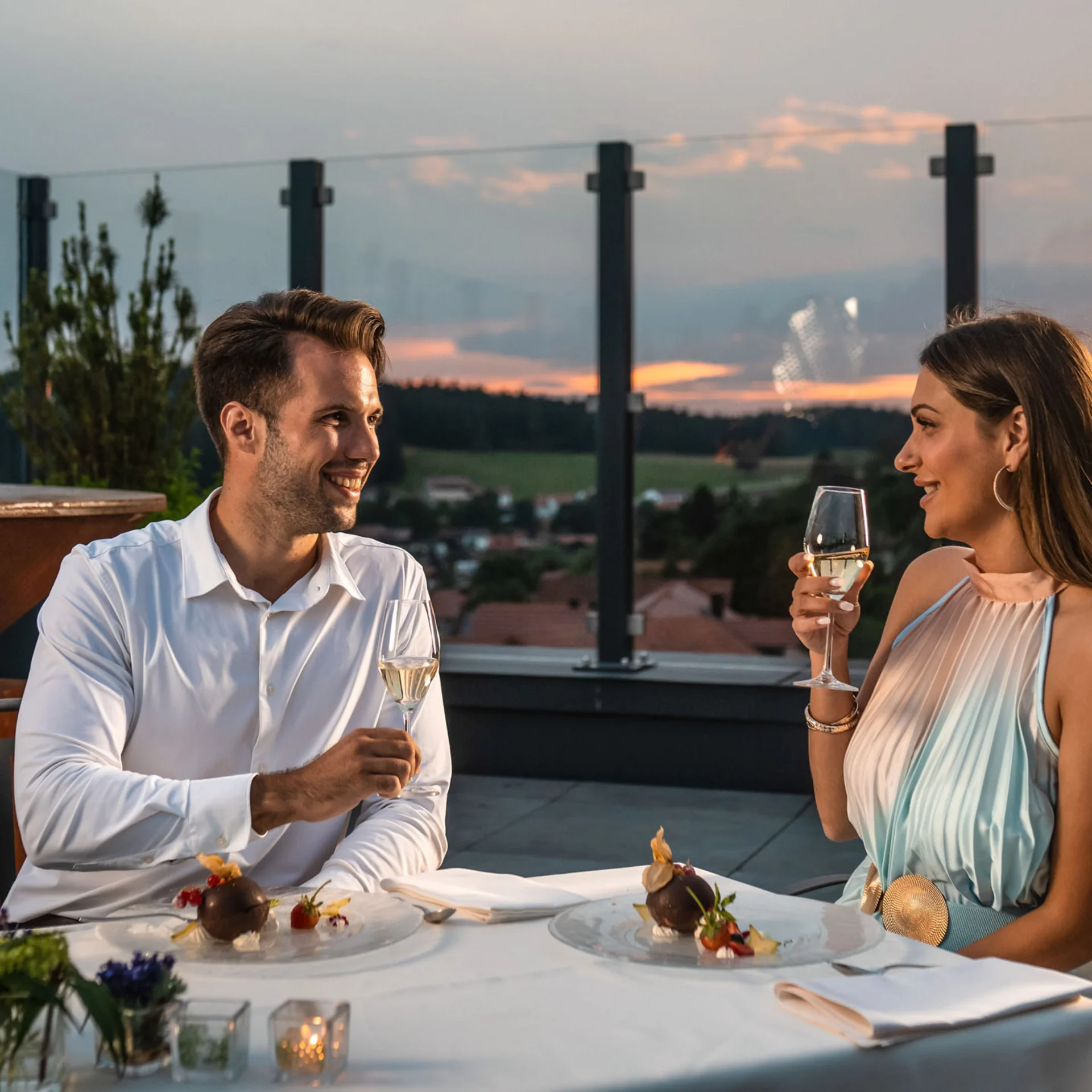 Paar genießt Abendessen und Champagner auf Terrasse bei Sonnenuntergang