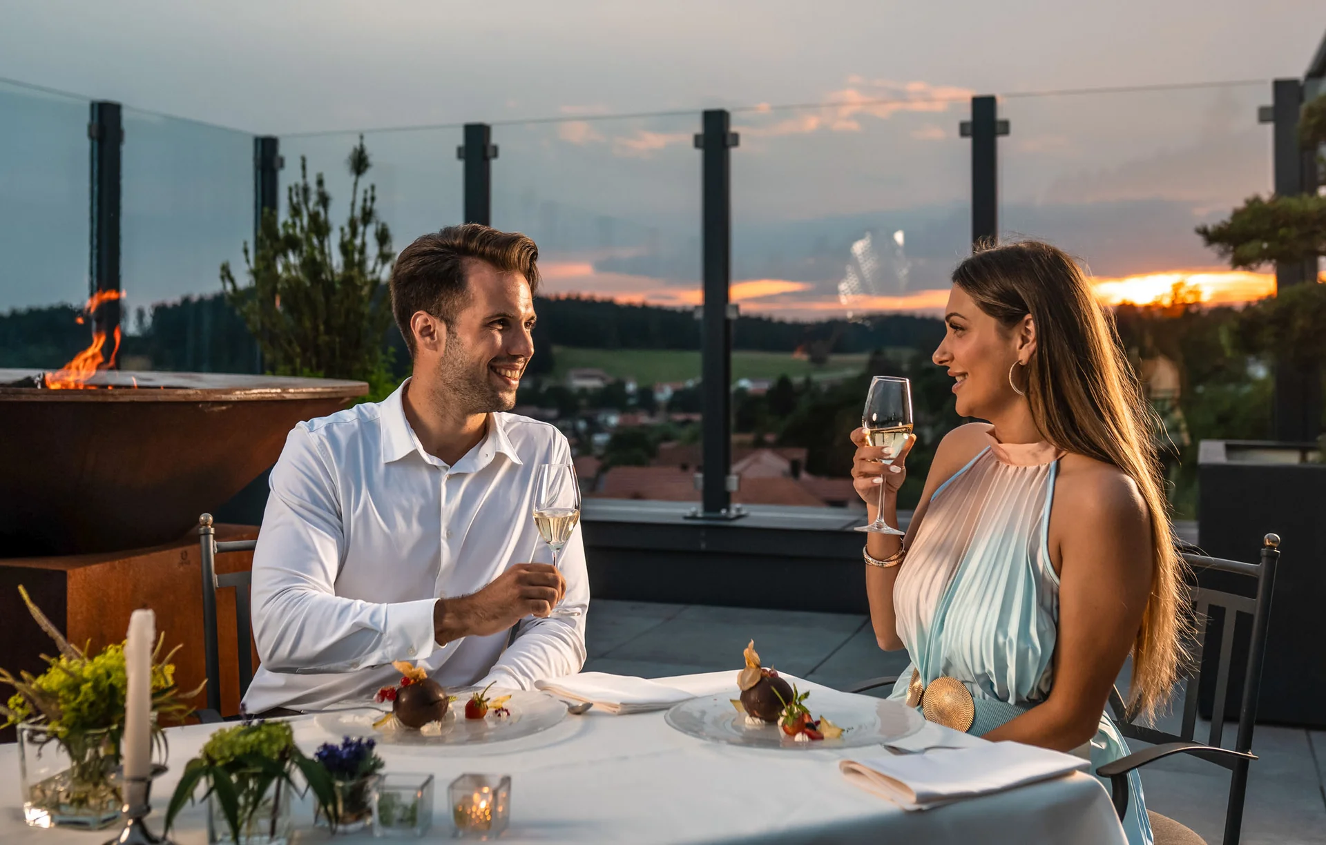 Paar genießt Abendessen und Champagner auf Terrasse bei Sonnenuntergang