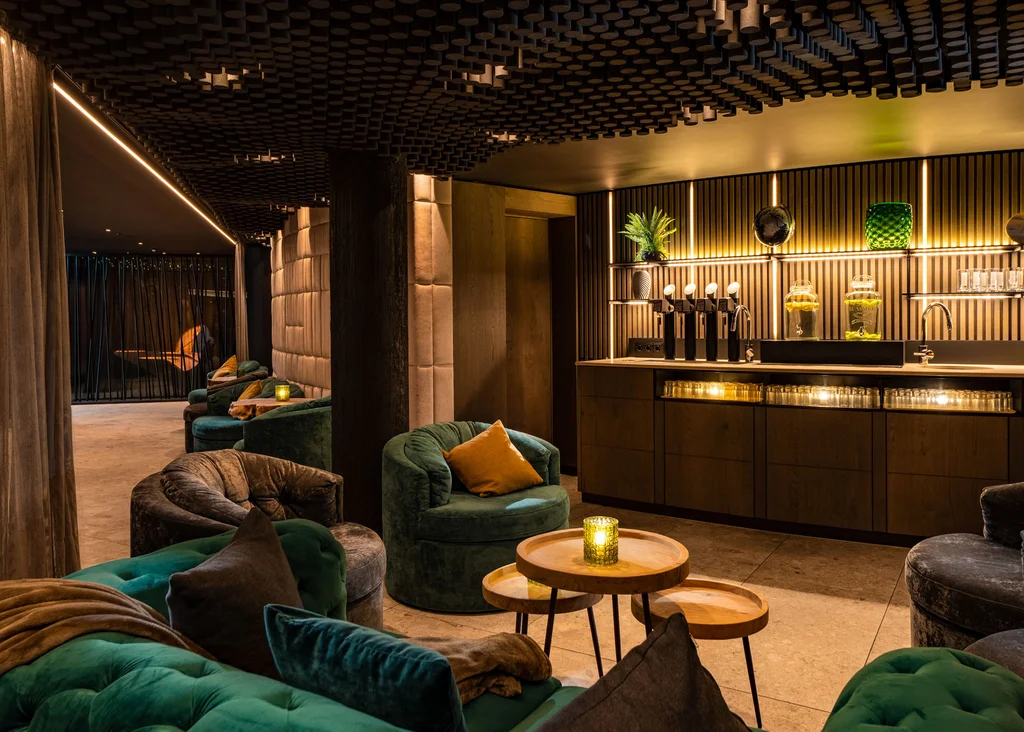Gemütliche Lounge mit grünen Sesseln und beleuchtetem Barbereich