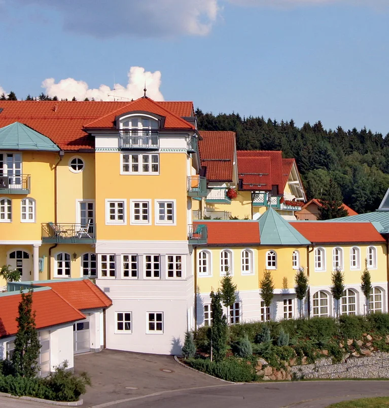 Großes gelbes Hotelgebäude mit roten Dächern vor Wald und blauem Himmel