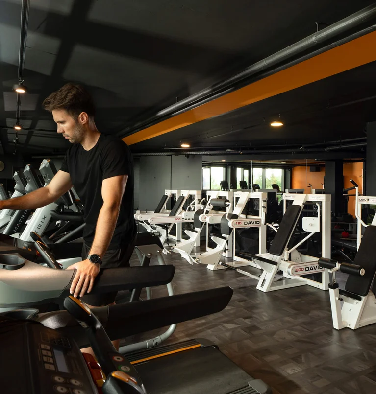 Mann bedient Laufband in einem modernen Fitnessstudio mit Trainingsgeräten