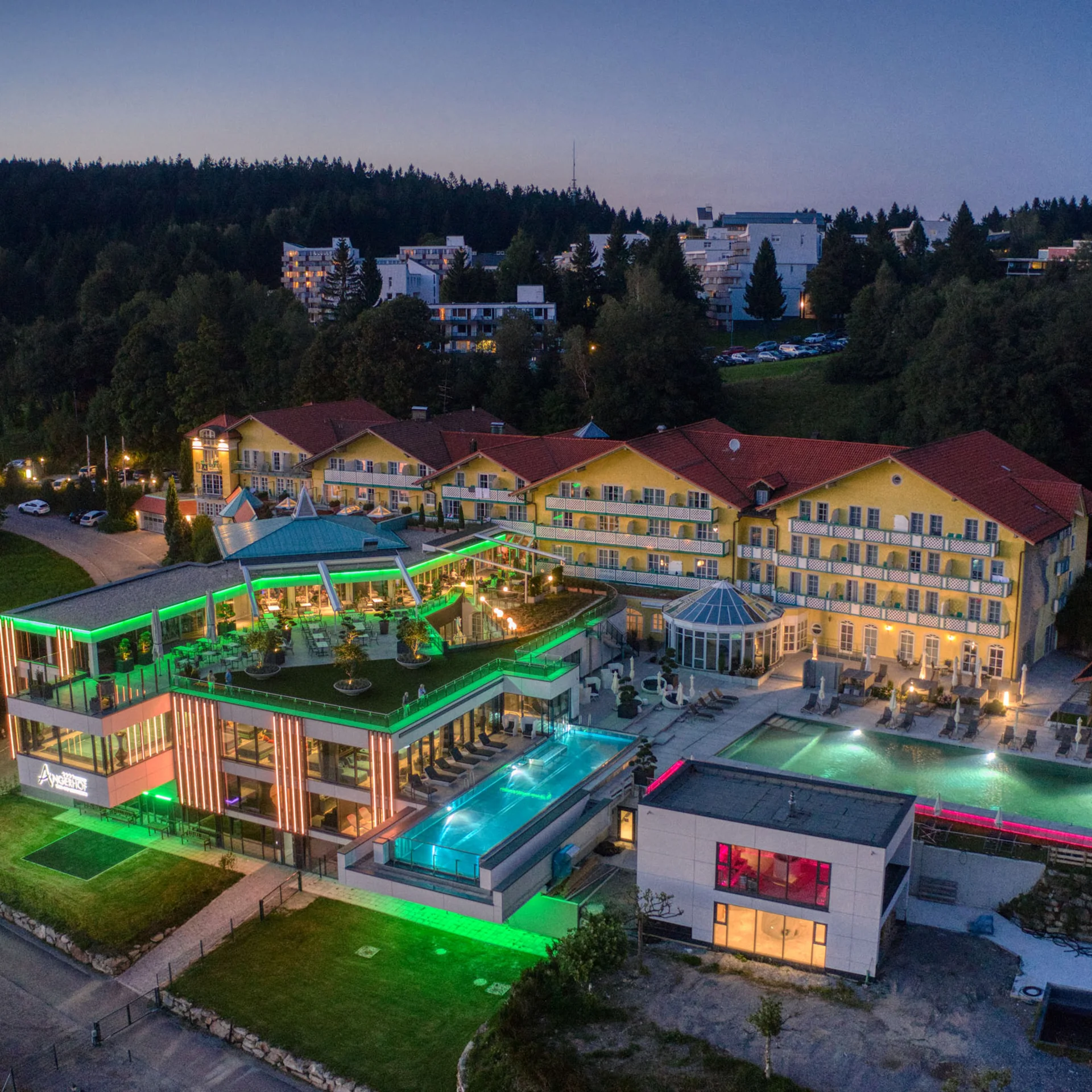 Modernes Hotel mit beleuchtetem Pool und umliegenden Gebäuden bei Abenddämmerung