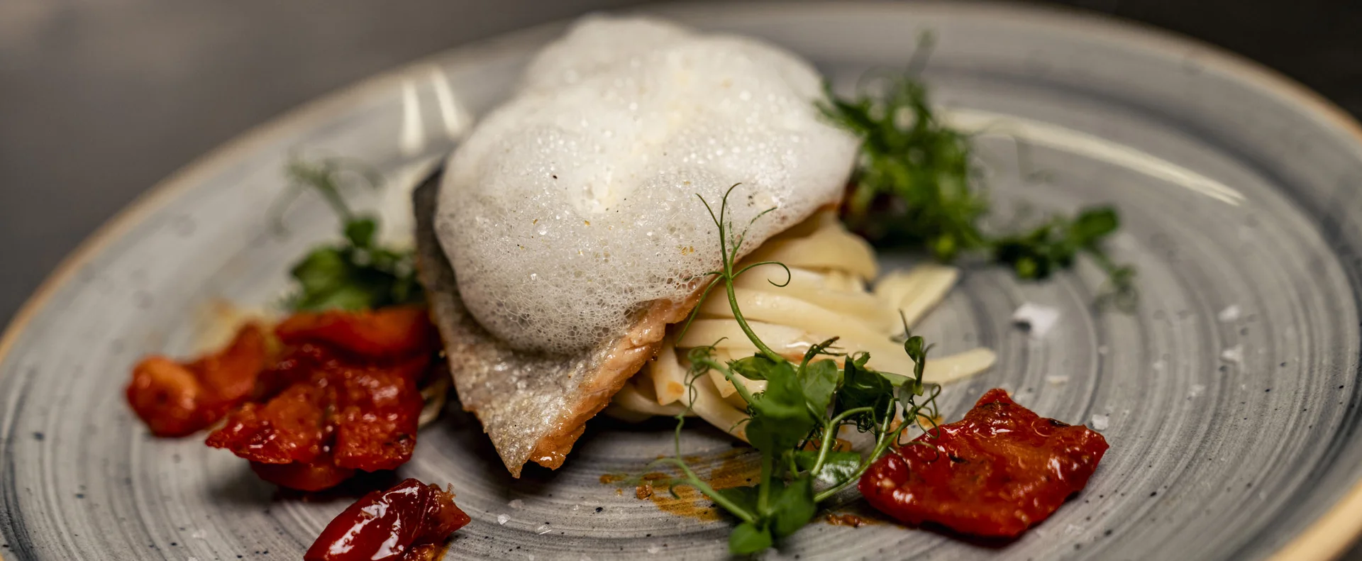Gourmetgericht mit Schaum, Kräutern und getrockneten Tomaten auf grauem Teller