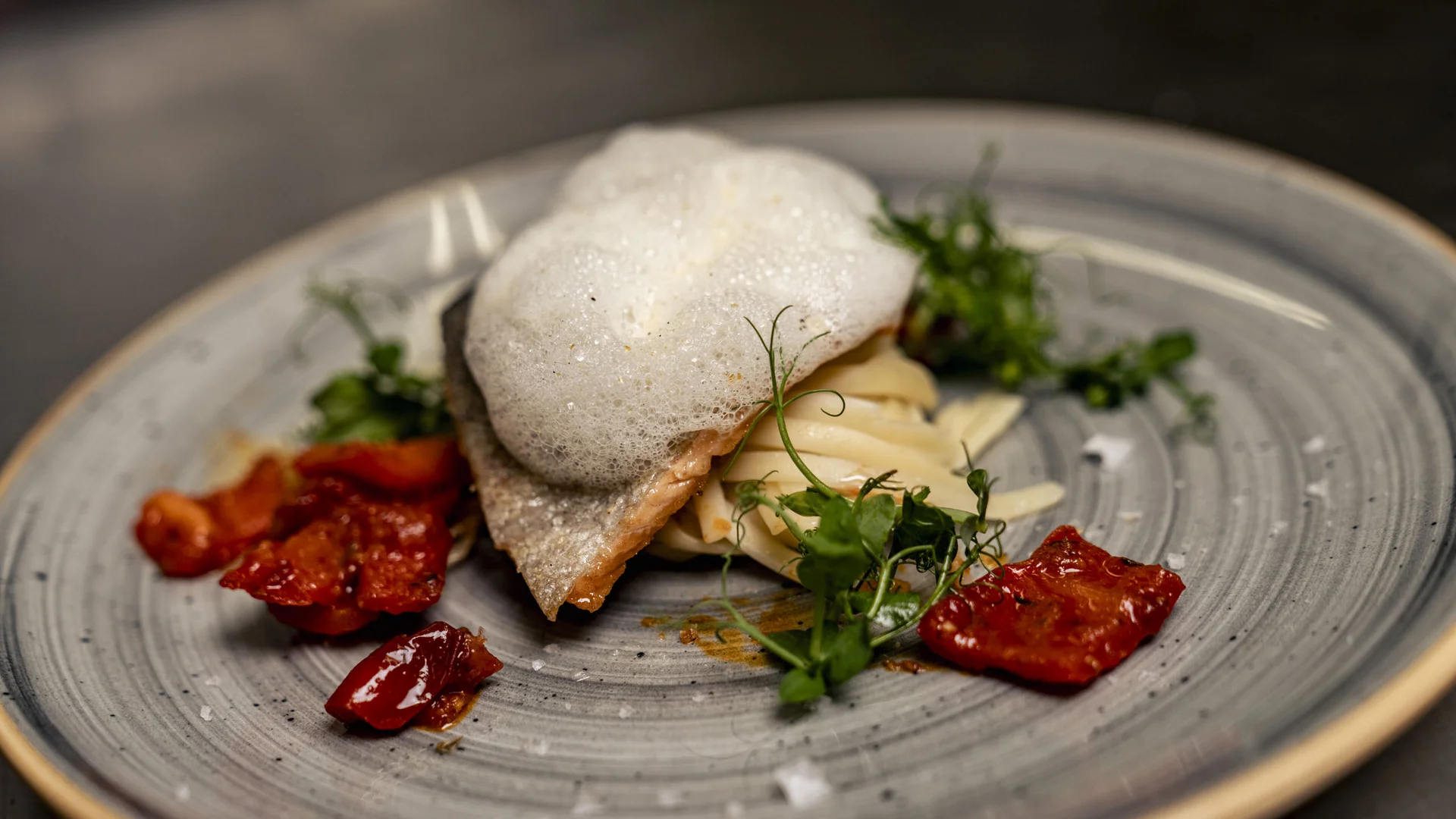 Gourmetgericht mit Schaum, Kräutern und getrockneten Tomaten auf grauem Teller