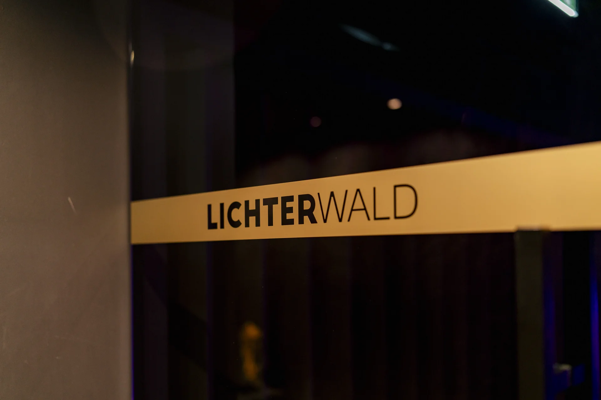 Gelbes Schild mit der Aufschrift LICHTERWALD an einer dunklen Wand