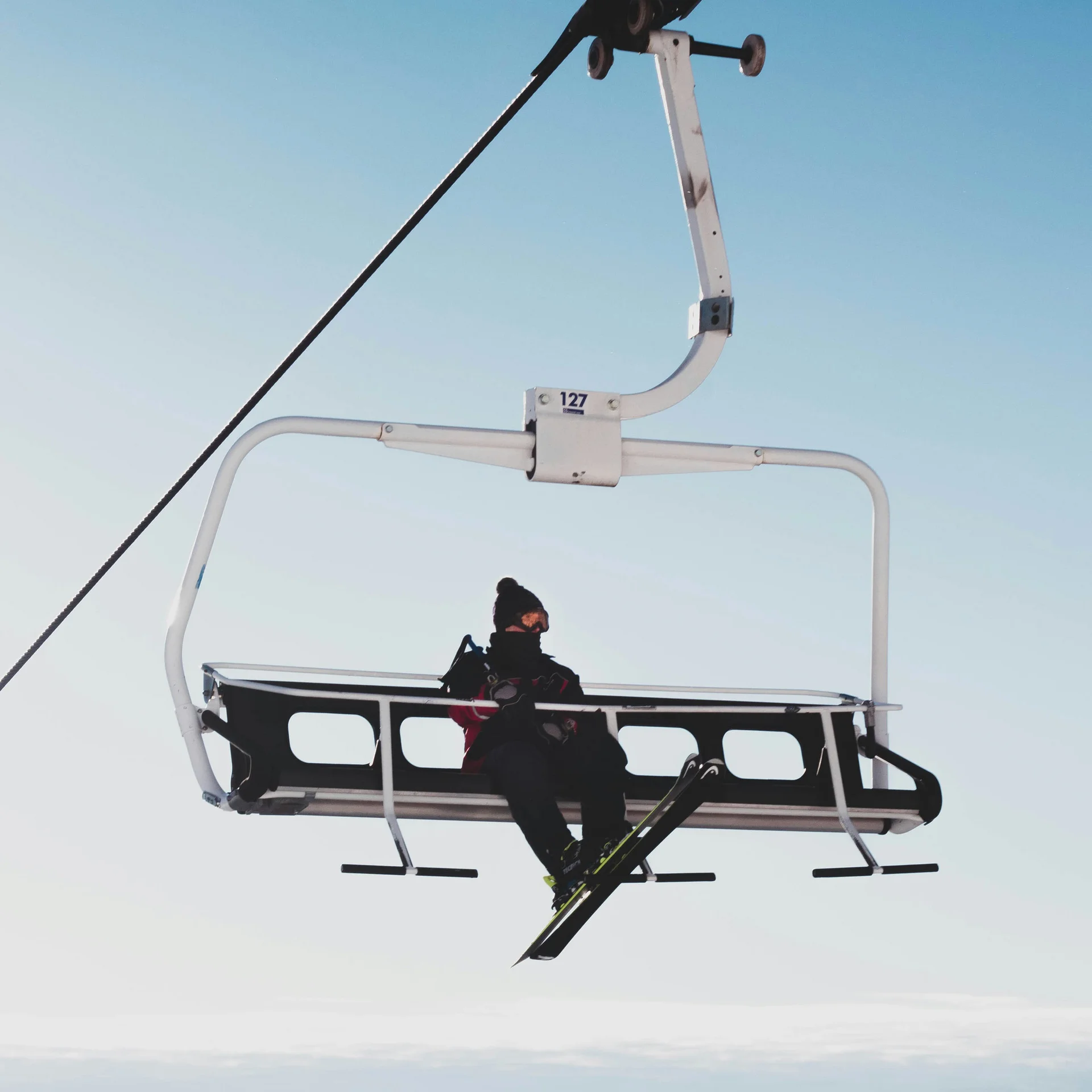 Skifahrer auf einem Sessellift vor klarem Himmel und Berglandschaft