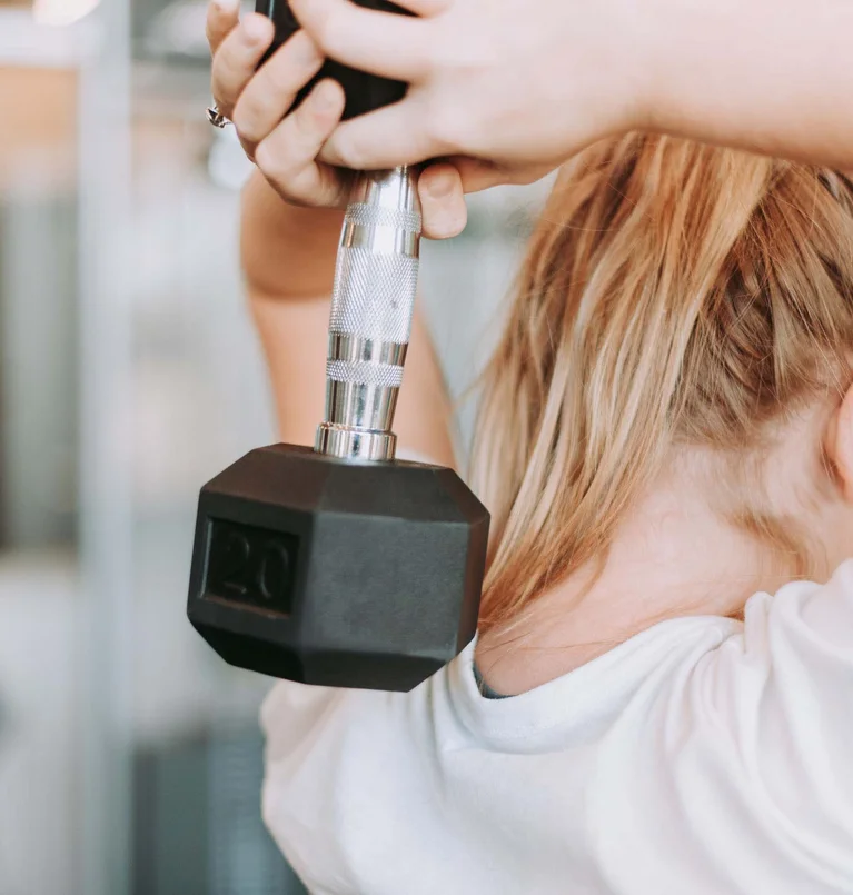 Frau trainiert Trizeps mit Kurzhantel im Fitnessstudio