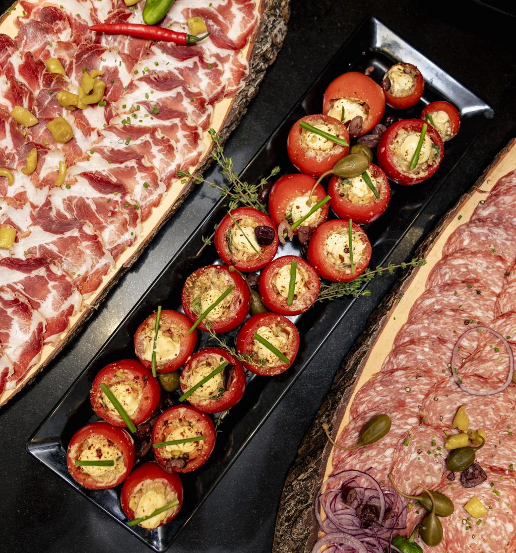 Teller mit verschiedenen Wurstscheiben und gefüllten Tomaten als Vorspeise