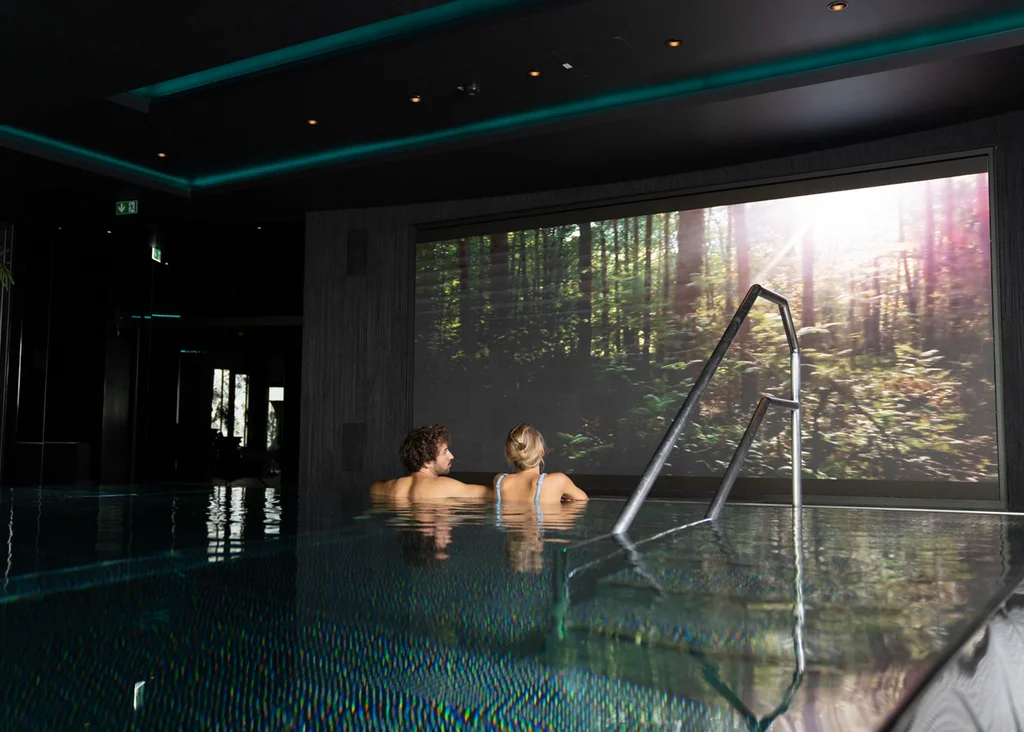 Paar entspannt im Innenpool mit großem Naturbild an der Wand