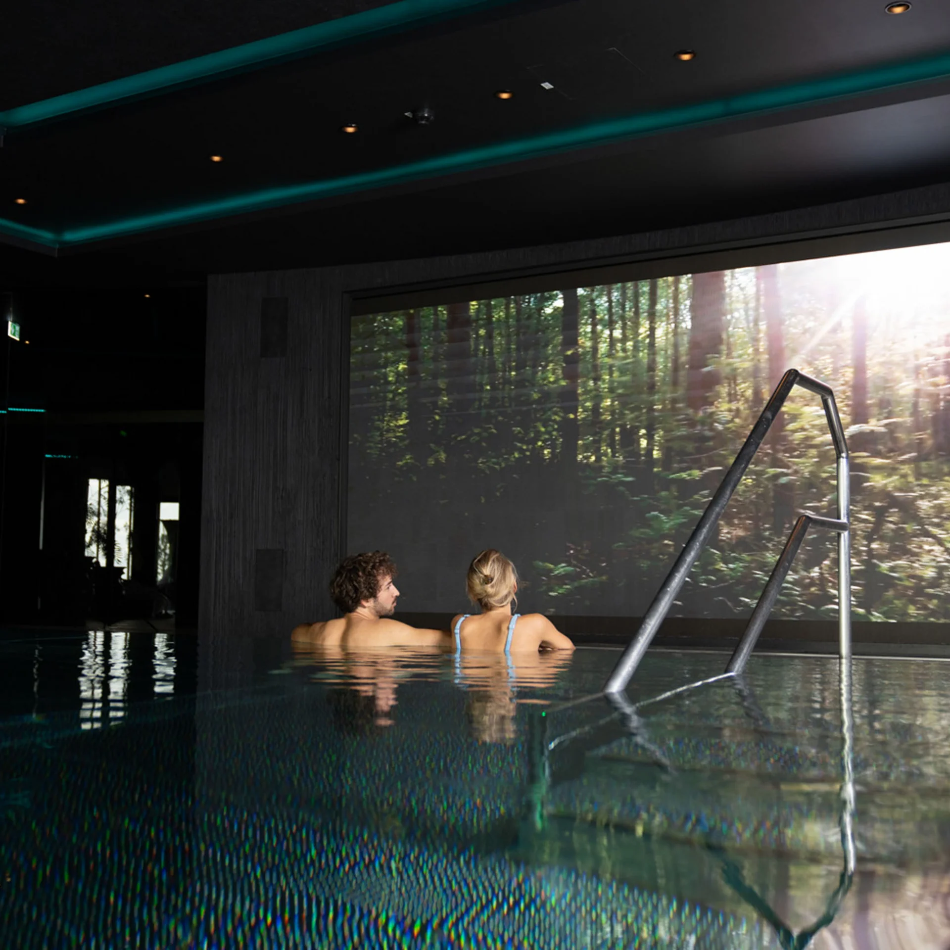 Paar entspannt im Innenpool mit großem Naturbild an der Wand