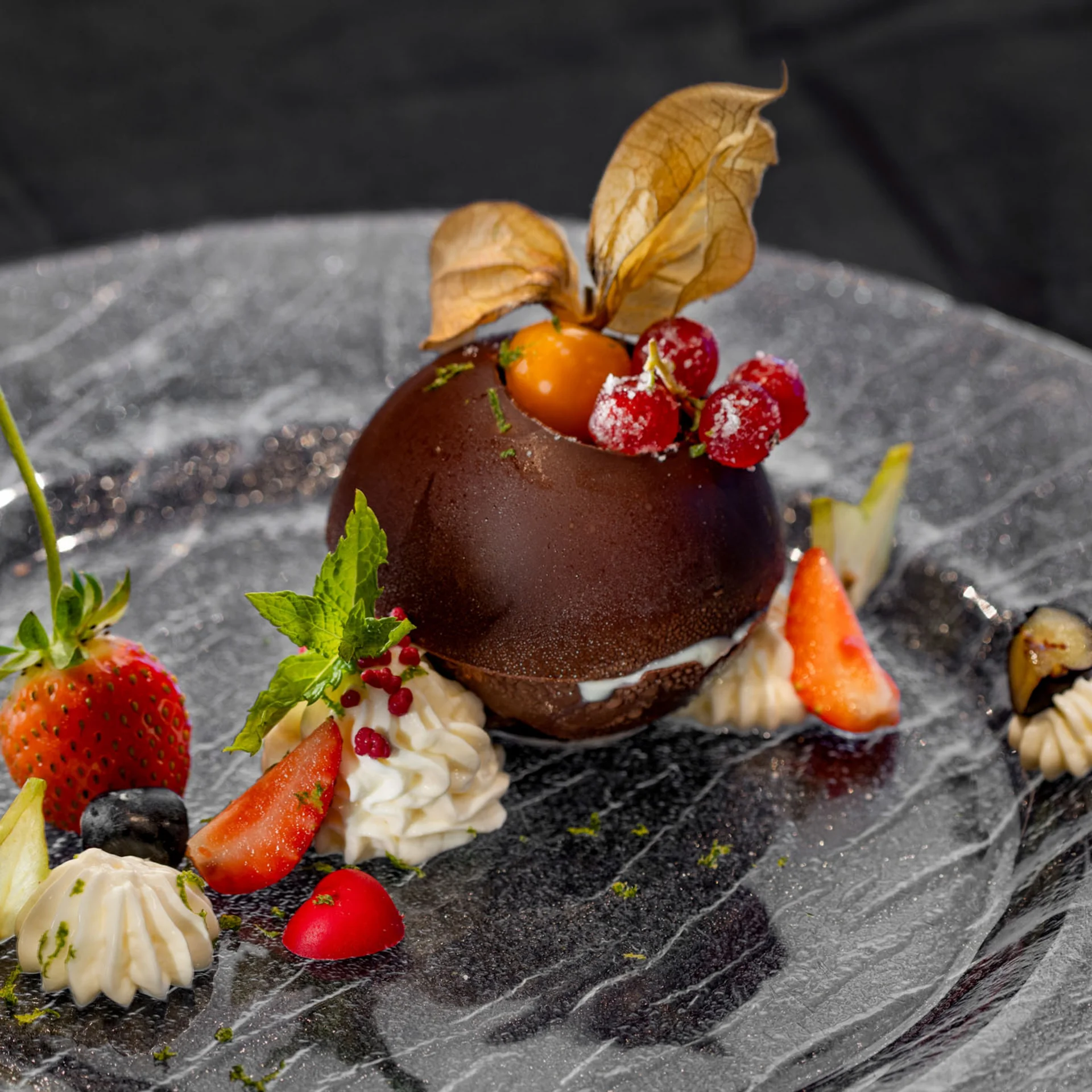 Schokoladendessert mit Beeren und Sahne auf schwarzem Teller dekoriert