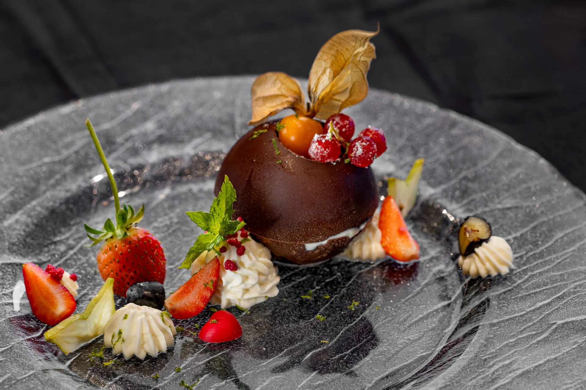 Schokoladendessert mit Beeren und Sahne auf schwarzem Teller dekoriert