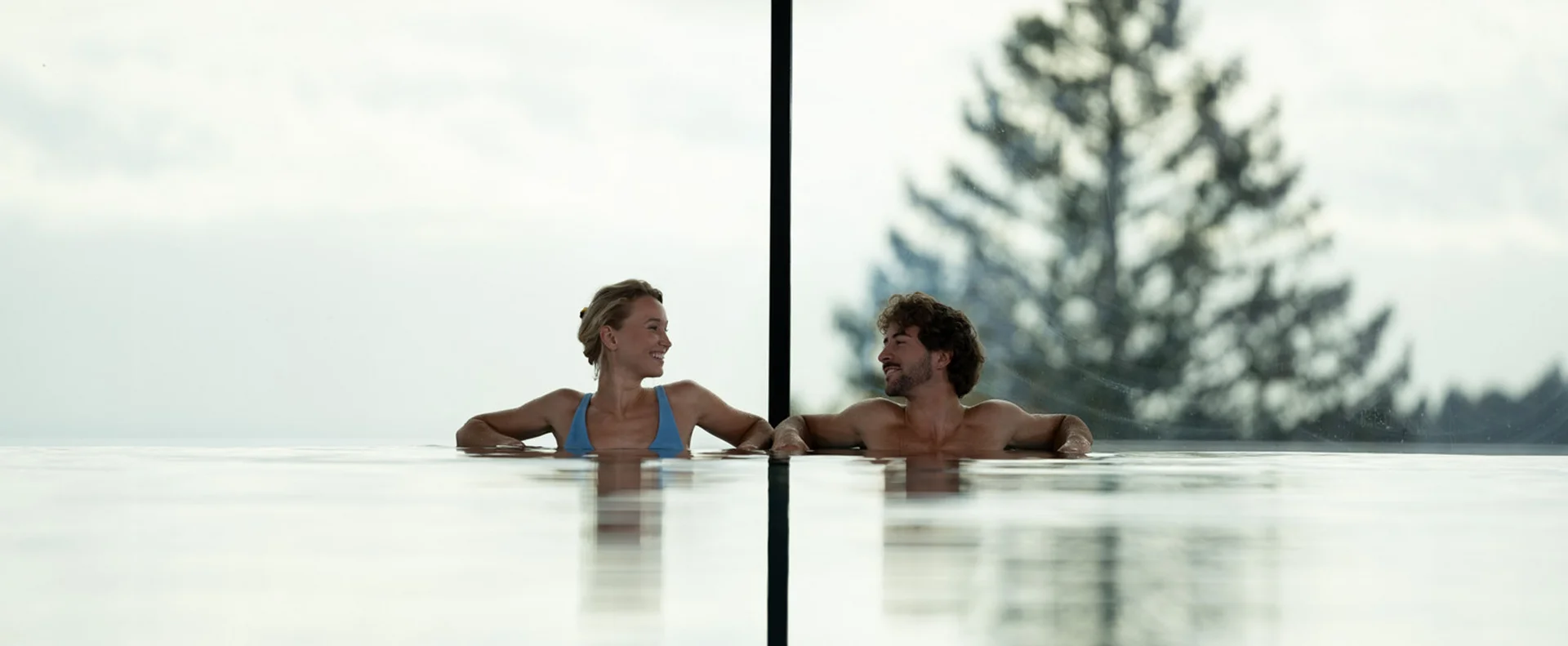 Zwei Personen entspannen in einem Pool mit Blick auf Bäume