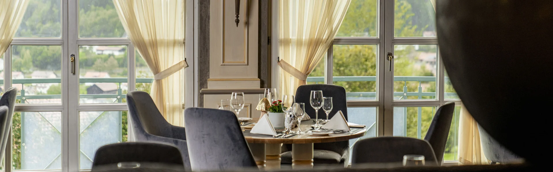 Restaurant mit gedecktem Tisch vor großen Fenstern und leichten Vorhängen
