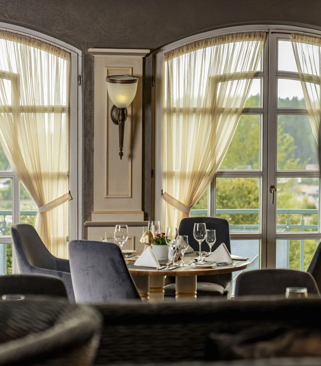 Restaurant mit gedecktem Tisch vor großen Fenstern und leichten Vorhängen