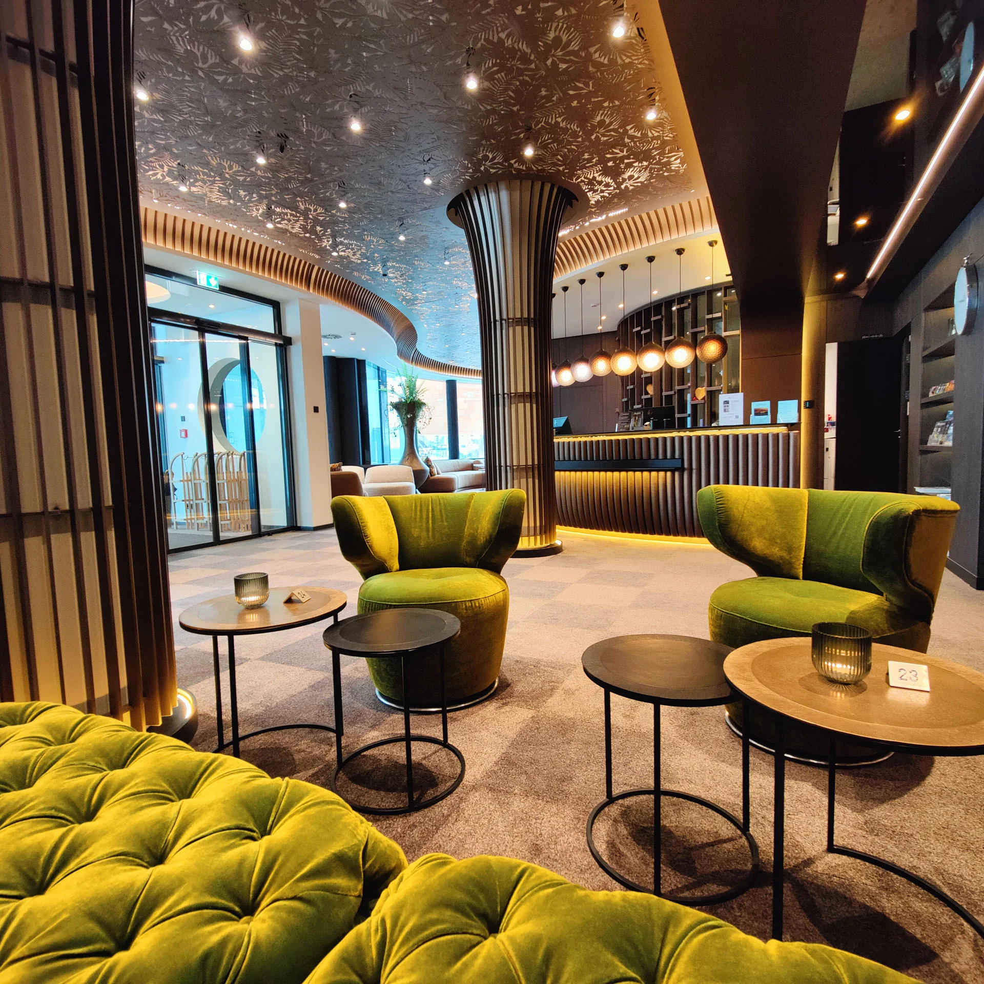 Modern eingerichteter Hotel-Lobby-Bereich mit grünen Sesseln und beleuchtetem Empfang