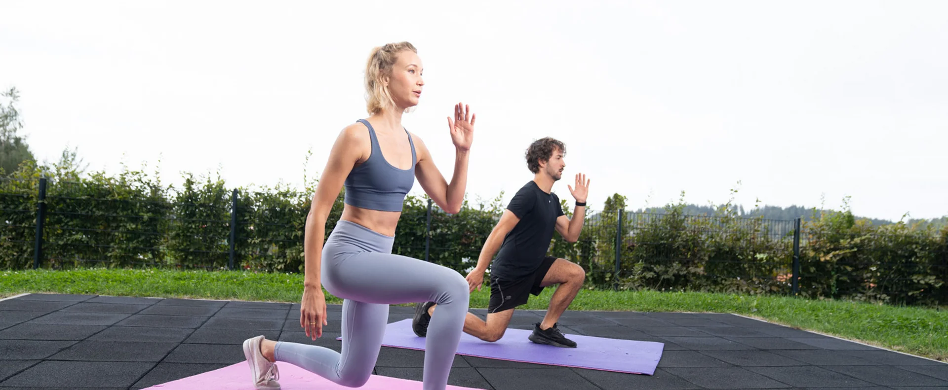 Frau und Mann machen Ausfallschritte auf Yogamatten im Freien
